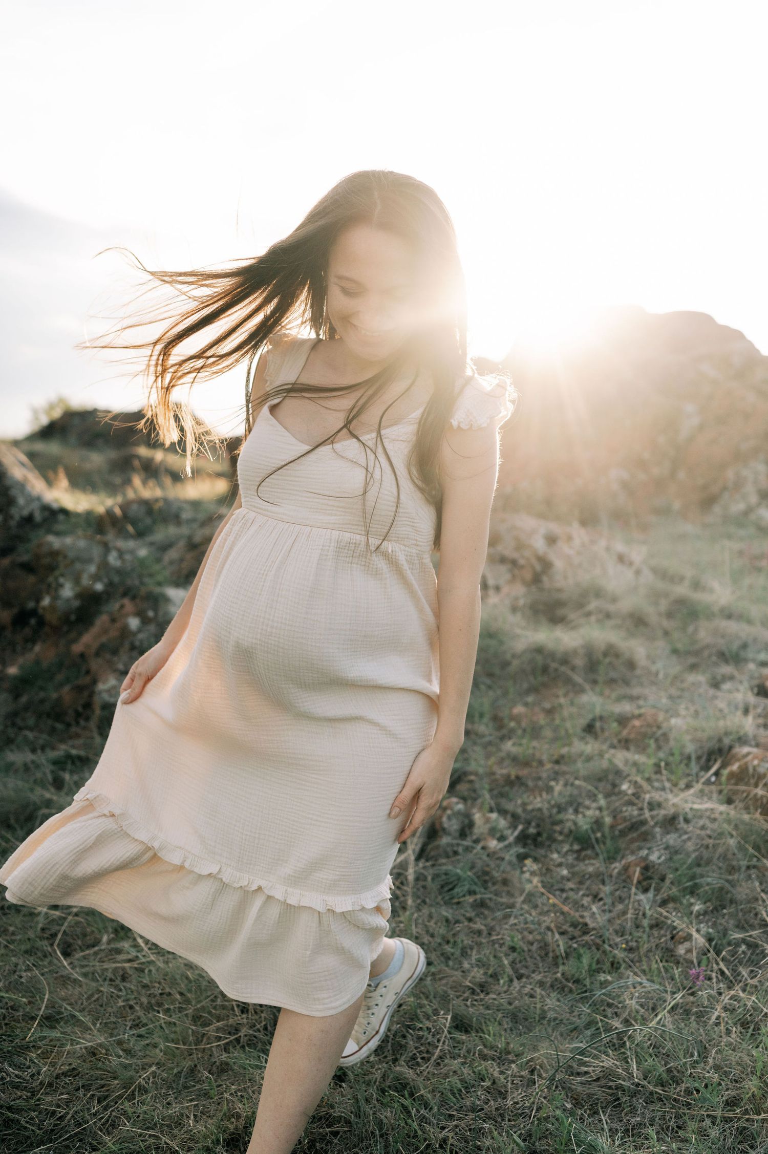 Ethereal white dress flowing in golden sunlight during sunset photoshoot in a grassy field.