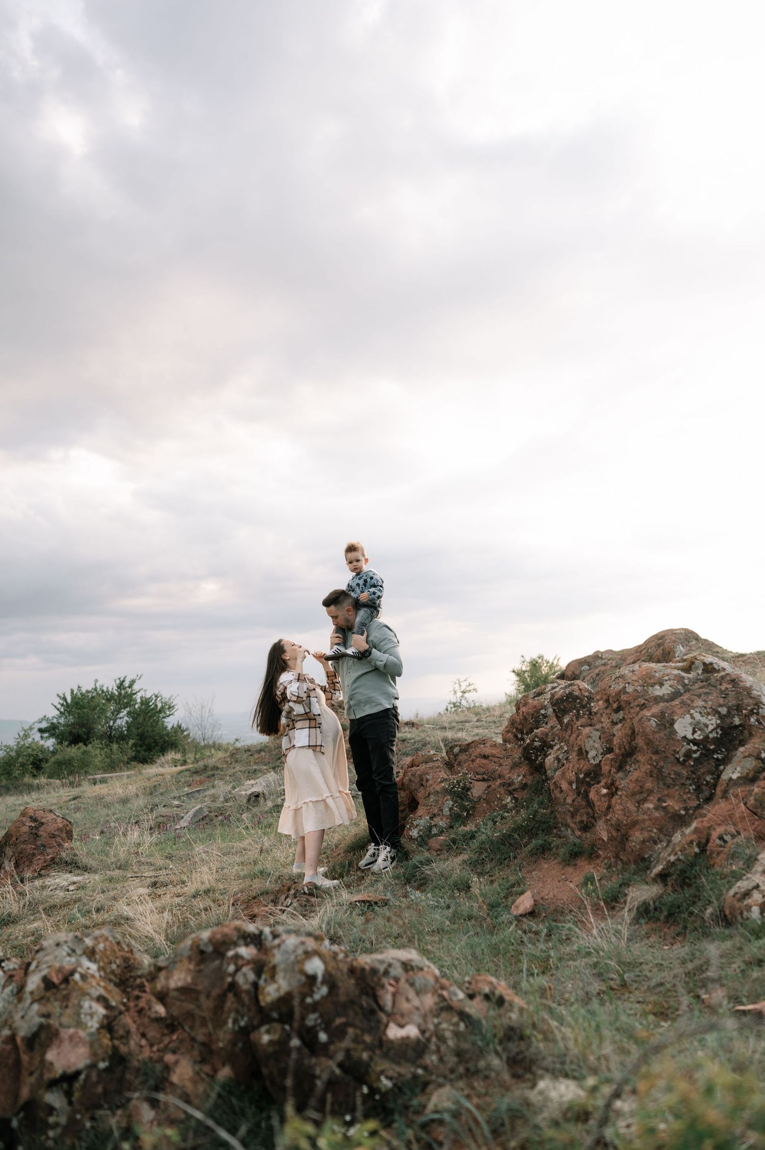 A couple embraces on a rocky hillside against a cloudy sky in a series of romantic outdoor portraits.