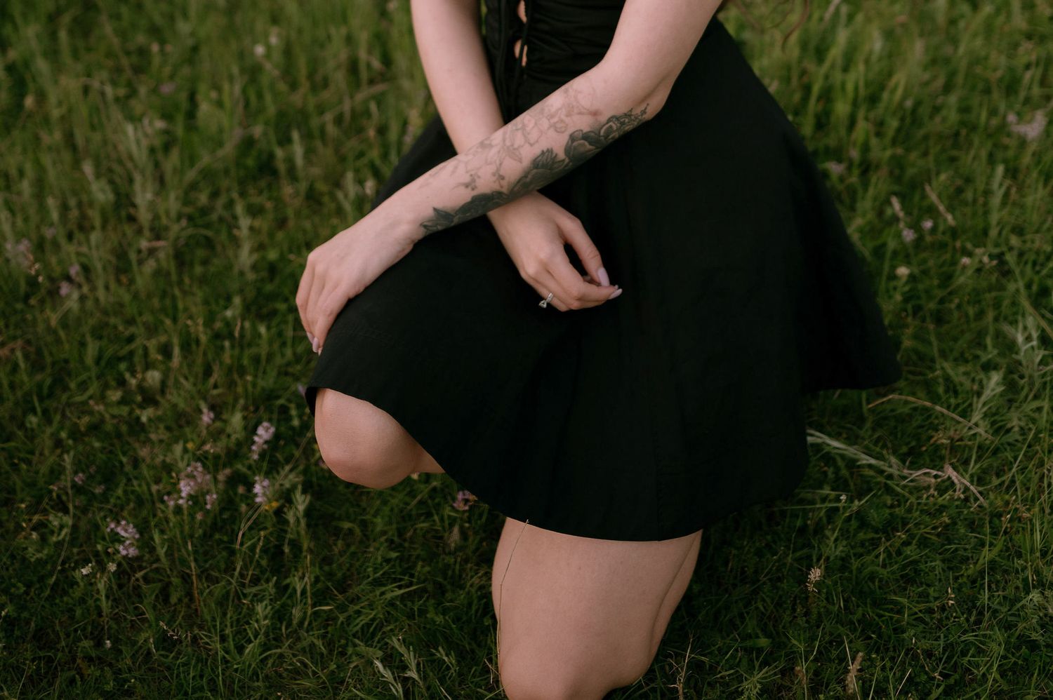 A person wearing a black dress stands in tall grass at sunset, creating a moody silhouette against nature.