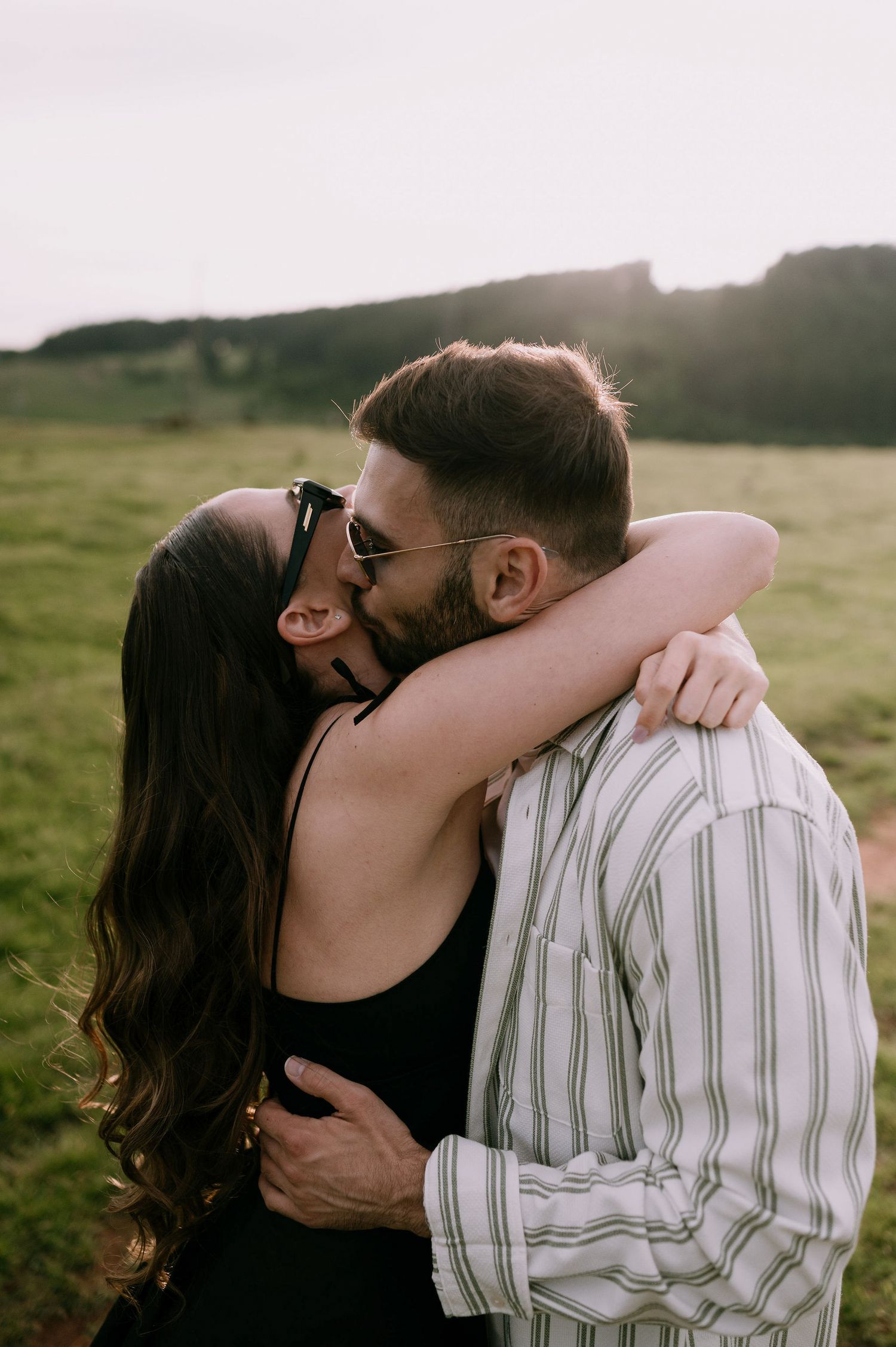 A romantic couple embraces and kisses in a series of intimate photos taken outdoors during golden hour.