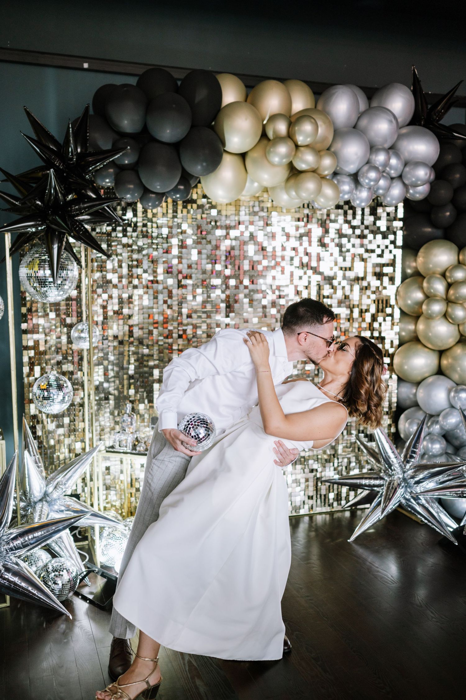 Elegant party scene with gold and silver balloons, sparkly backdrop, and white decor creating a glamorous atmosphere.