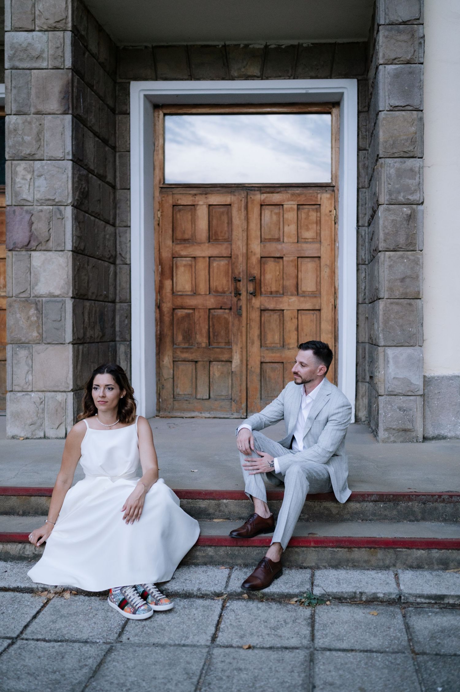 A couple in wedding attire sits playfully on stone steps in a series of connected photos showing different poses.