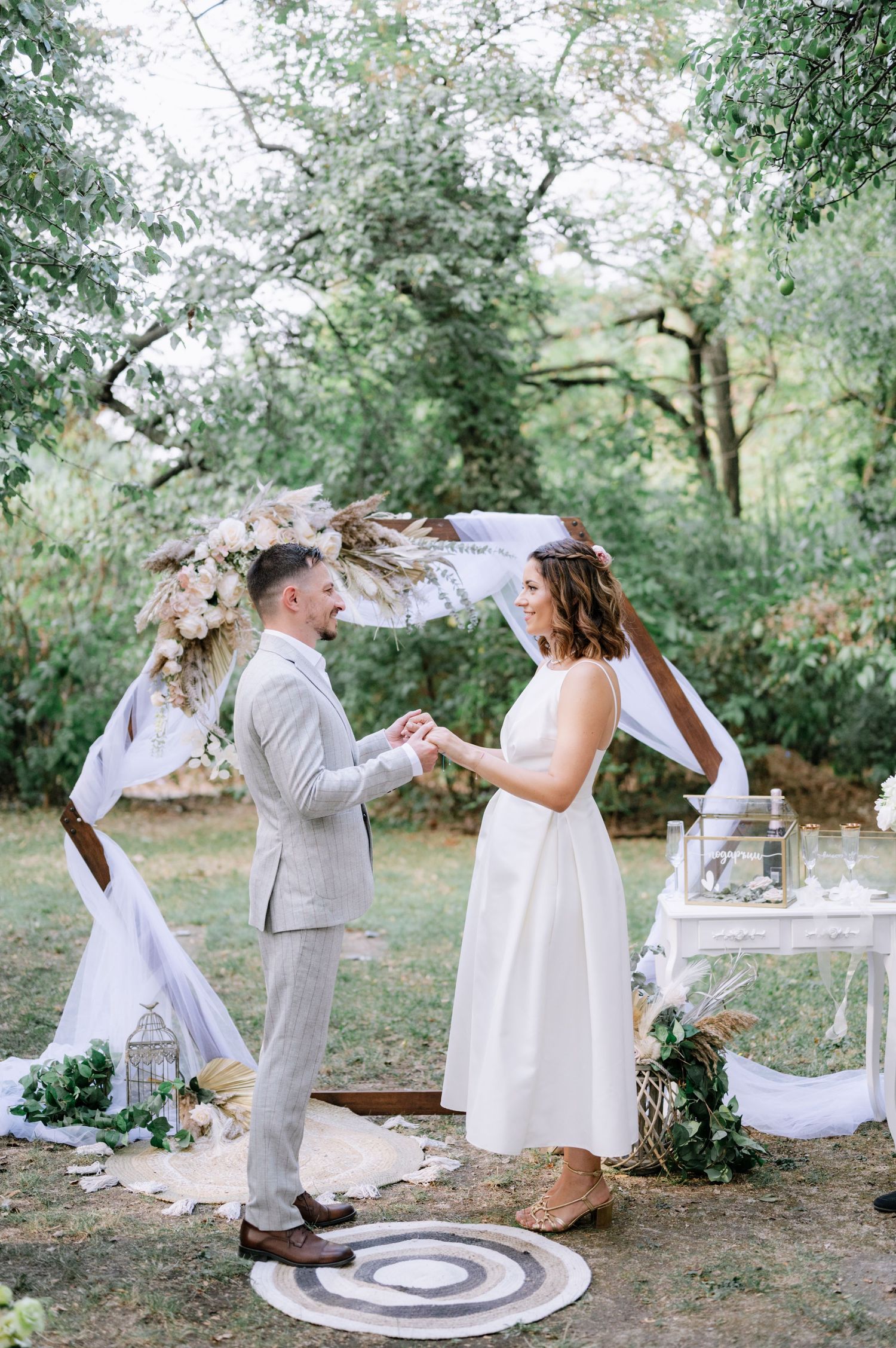 A couple exchanges vows during an intimate outdoor woodland wedding ceremony under a floral arch with rustic decor.