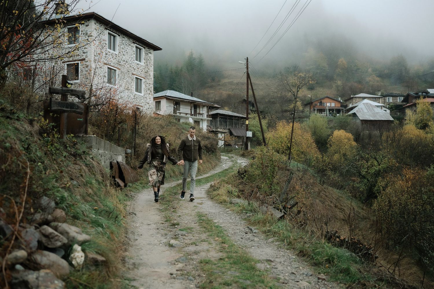 Foggy rural landscape with traditional stone buildings and autumn foliage in a remote mountain setting.