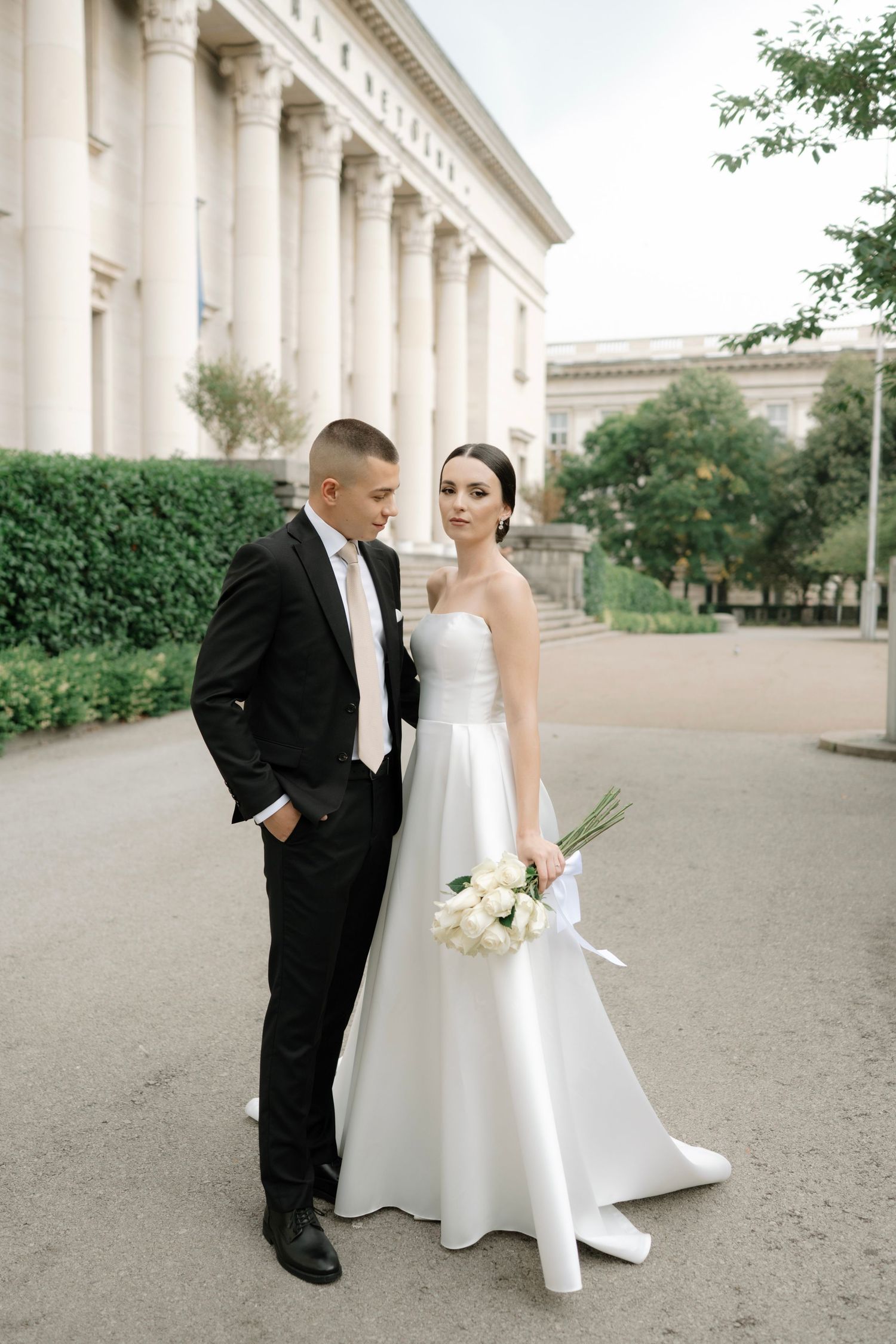 Elegant wedding couple poses together in front of a grand building with white columns.