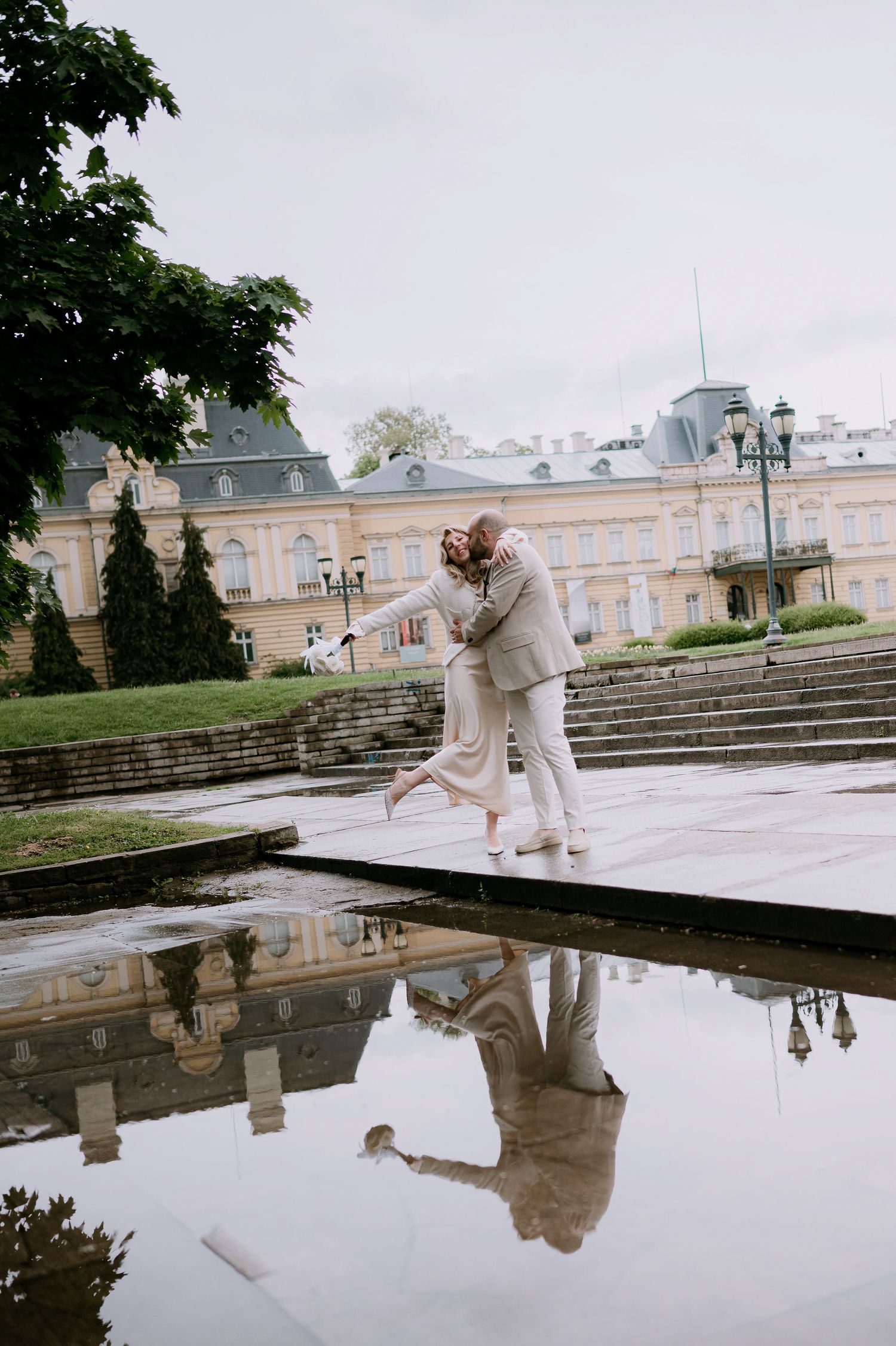 Dancers in beige outfits perform elegant moves by palace reflecting pool.