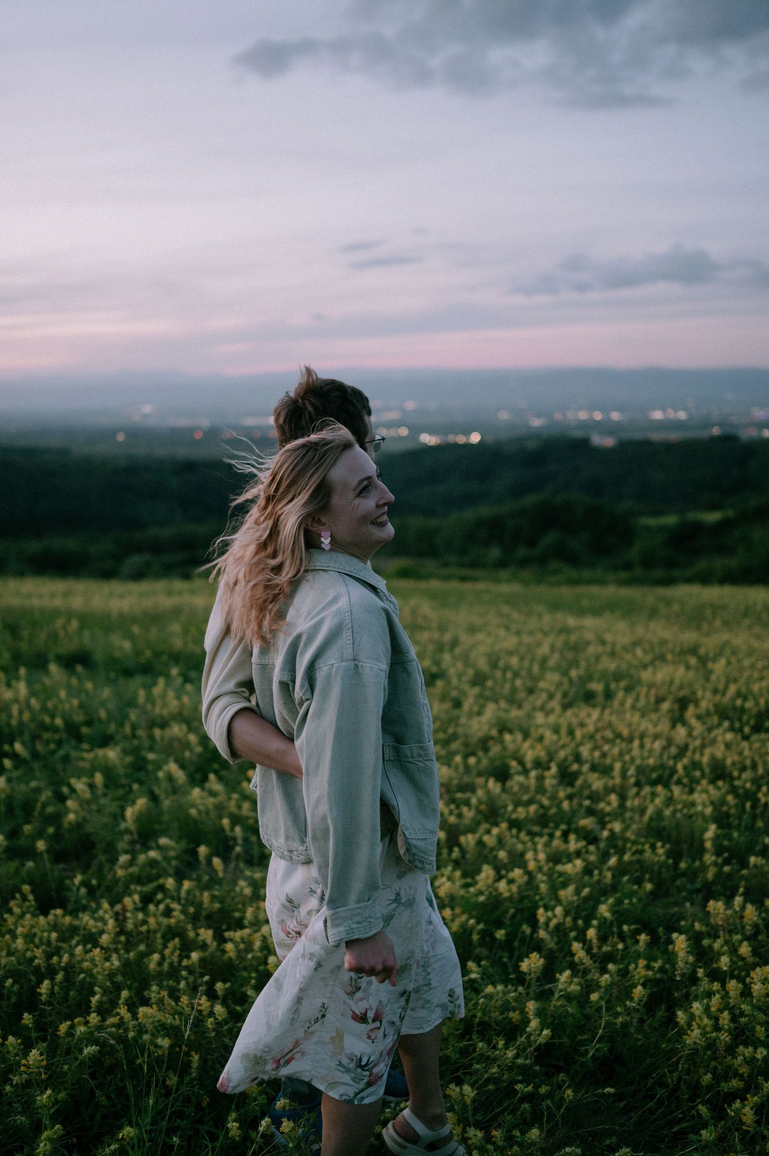 A couple dances playfully in a blooming yellow flower field at sunset.