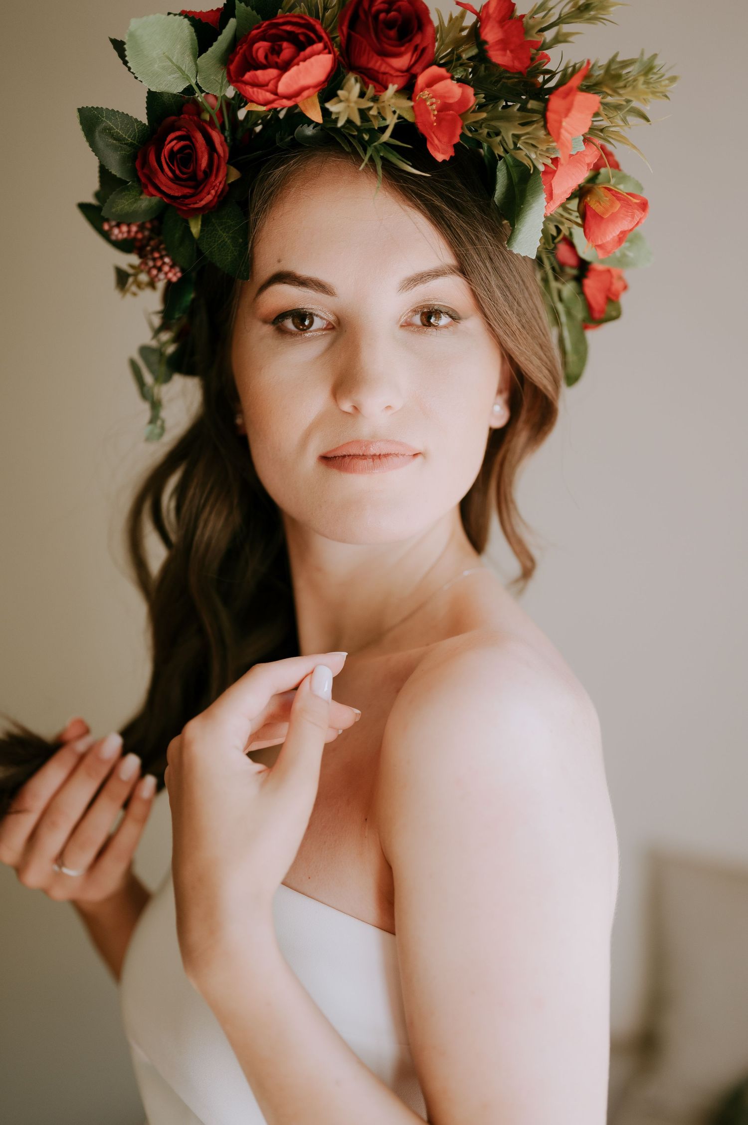 Elegant bridal portrait with red rose crown and white strapless gown in warm lighting.