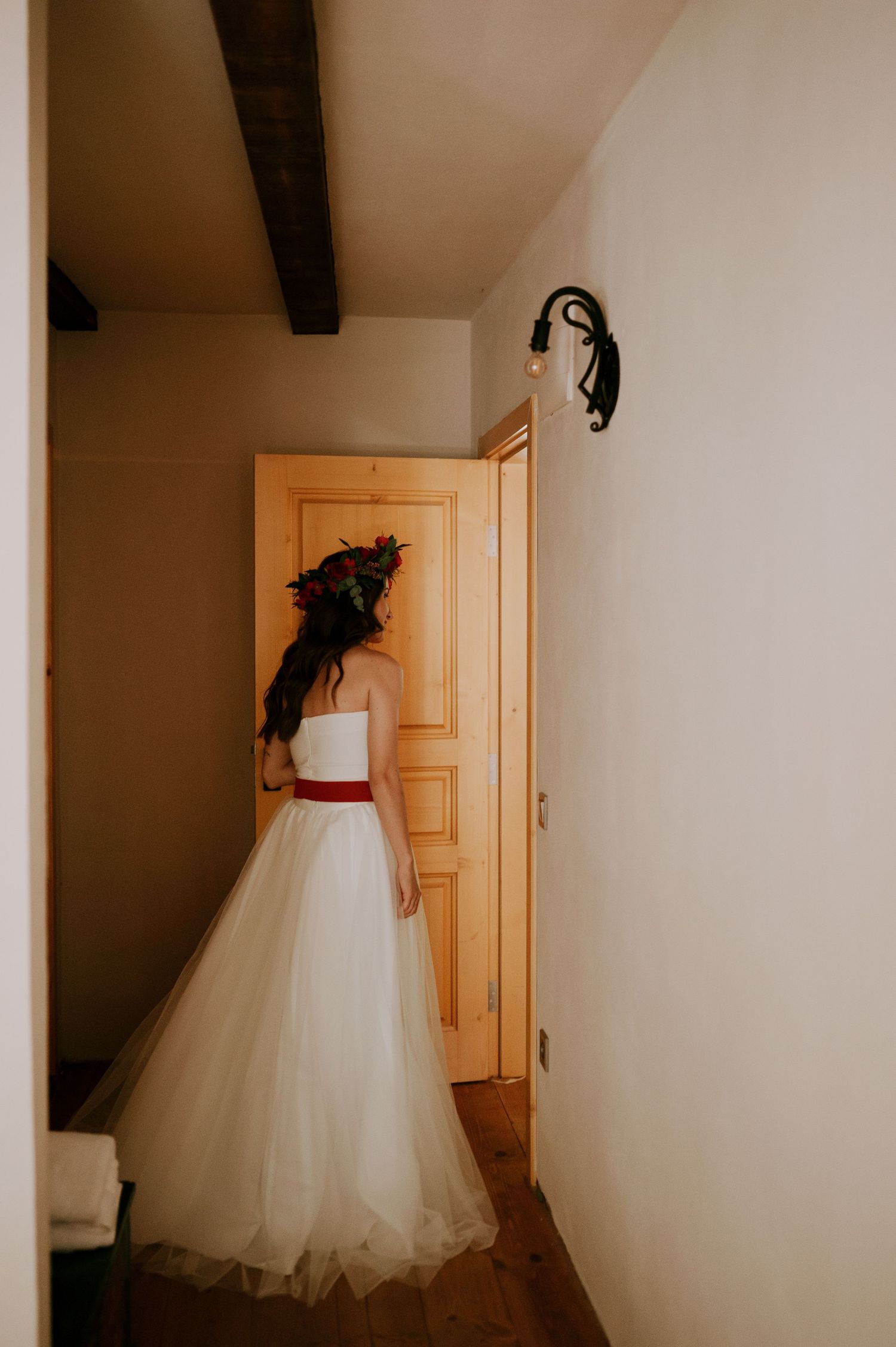A white wedding dress hangs elegantly in a hallway with wooden doors.