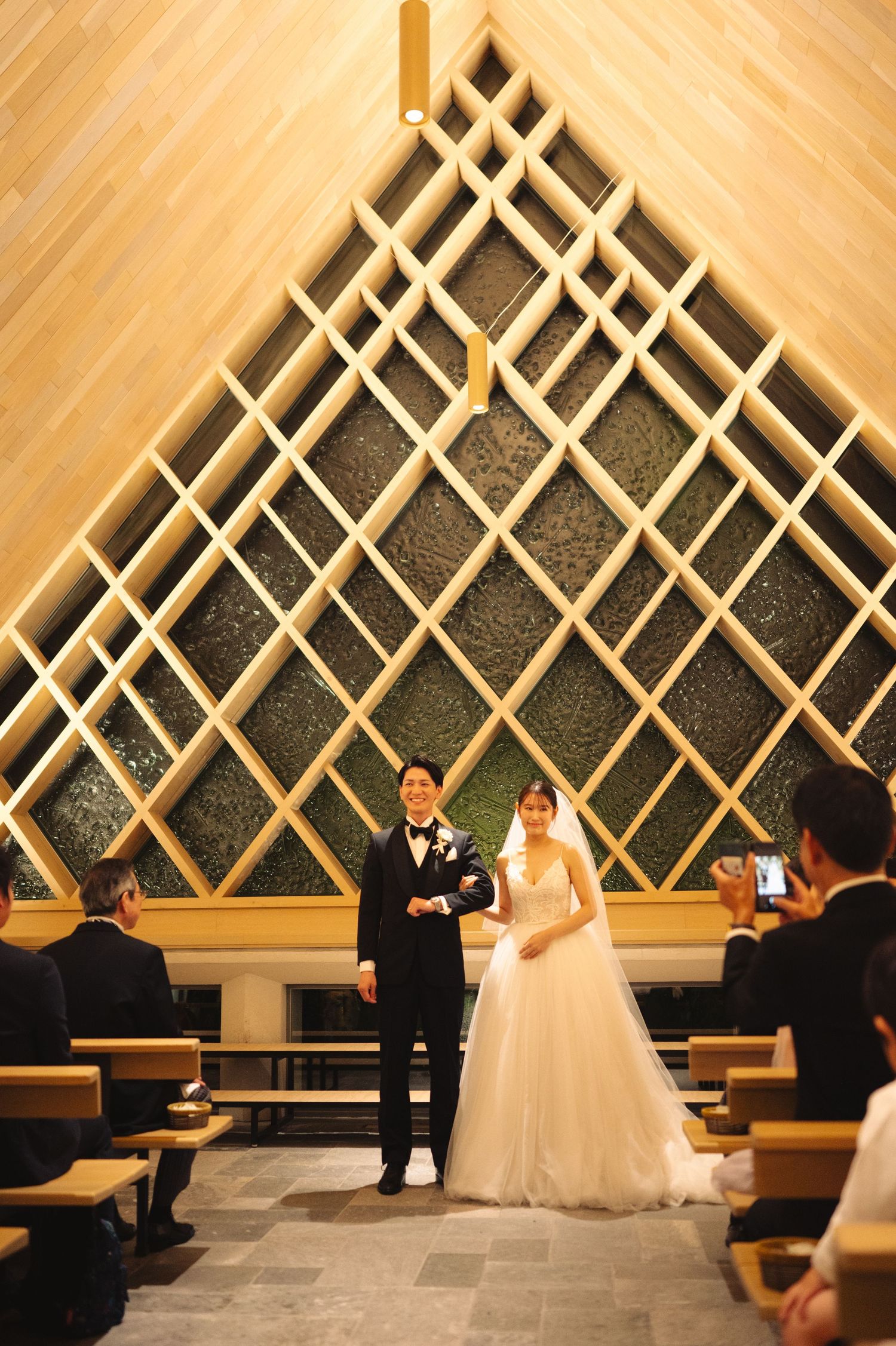 A couple stands at the altar of a modern chapel with dramatic diamond lattice wall design.