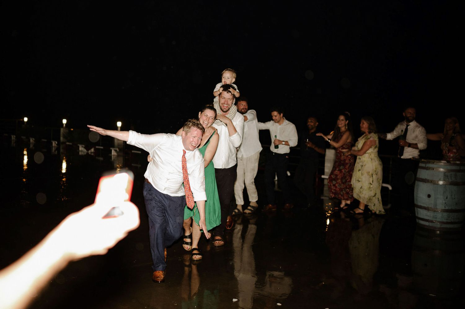 Large group of people dancing with raised arms at a nighttime celebration.