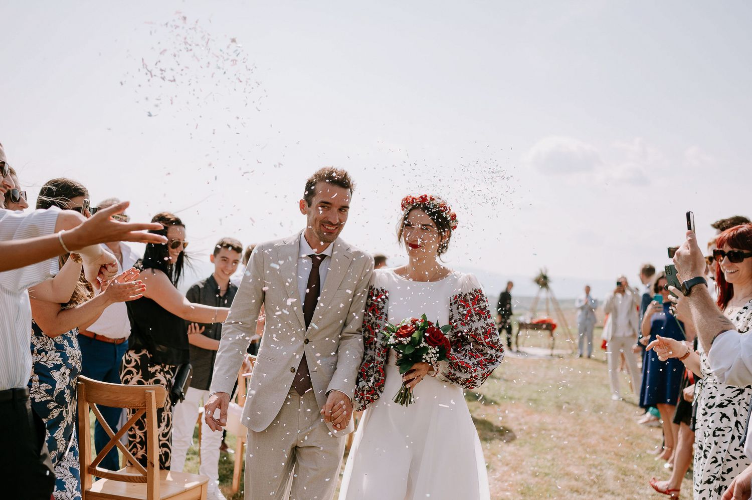 A joyful wedding ceremony exit with guests showering confetti on a couple walking down an outdoor aisle.