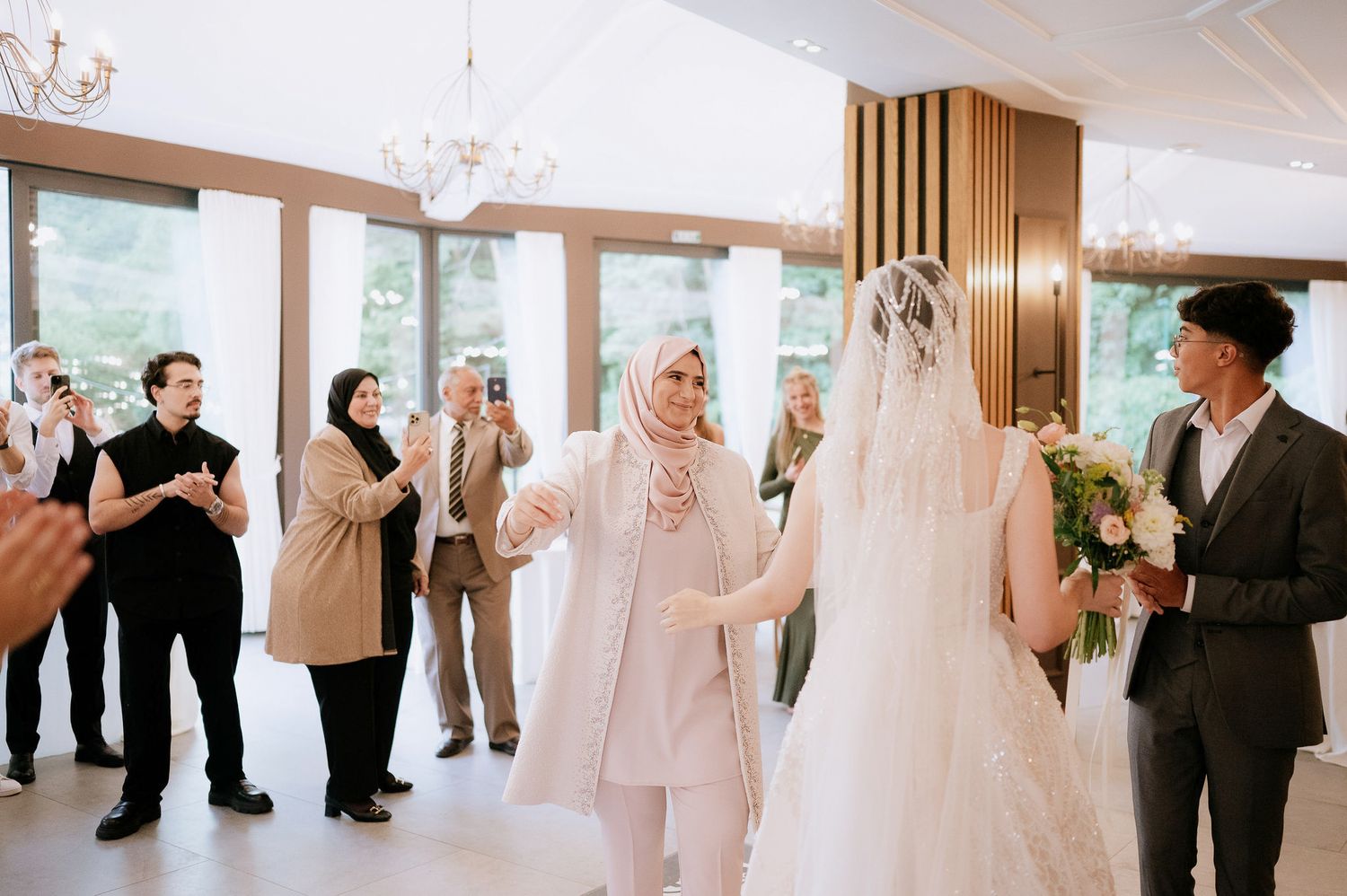 Wedding guests gather in a bright reception hall with wooden accents and modern lighting.