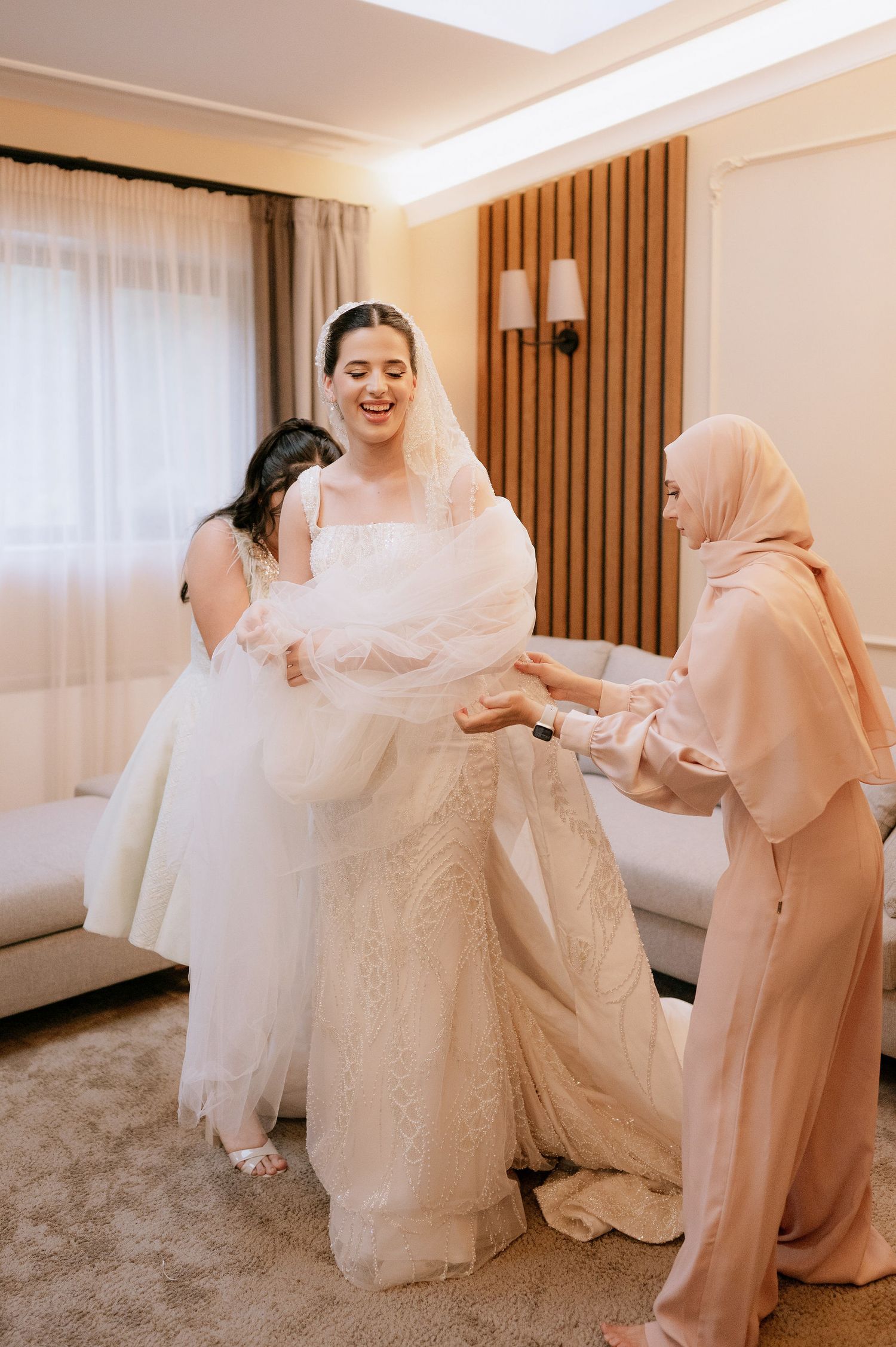Joyful pre-wedding moments as attendants assist with arranging a beautiful white wedding dress.