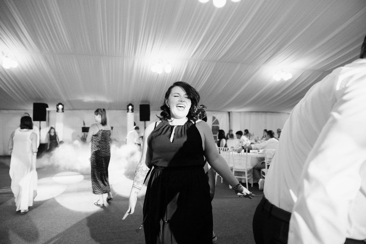 Black and white photo of wedding guests dancing in a tent venue.