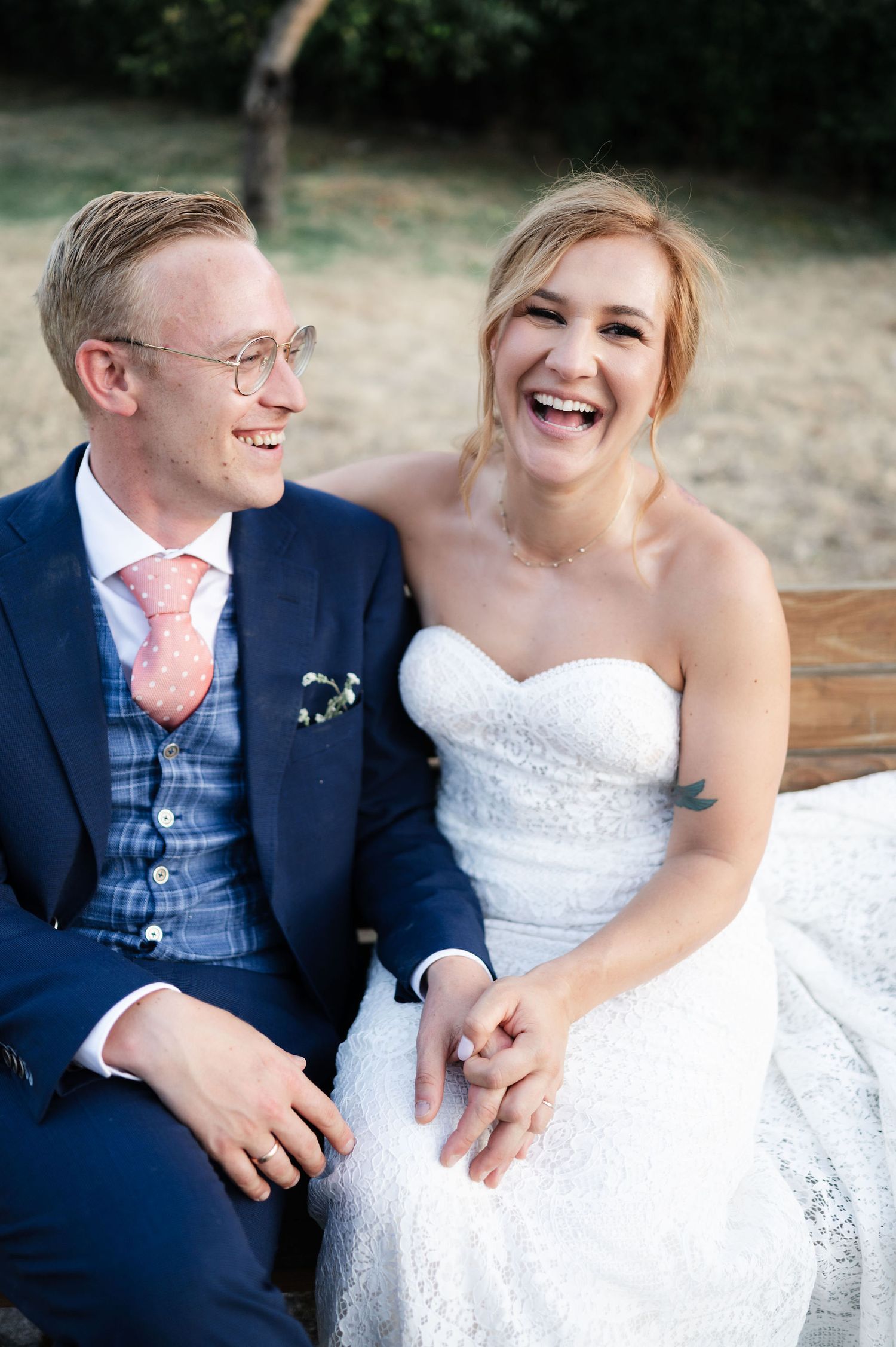 Wedding portrait showing joyful moment between newlyweds sitting together outdoors.