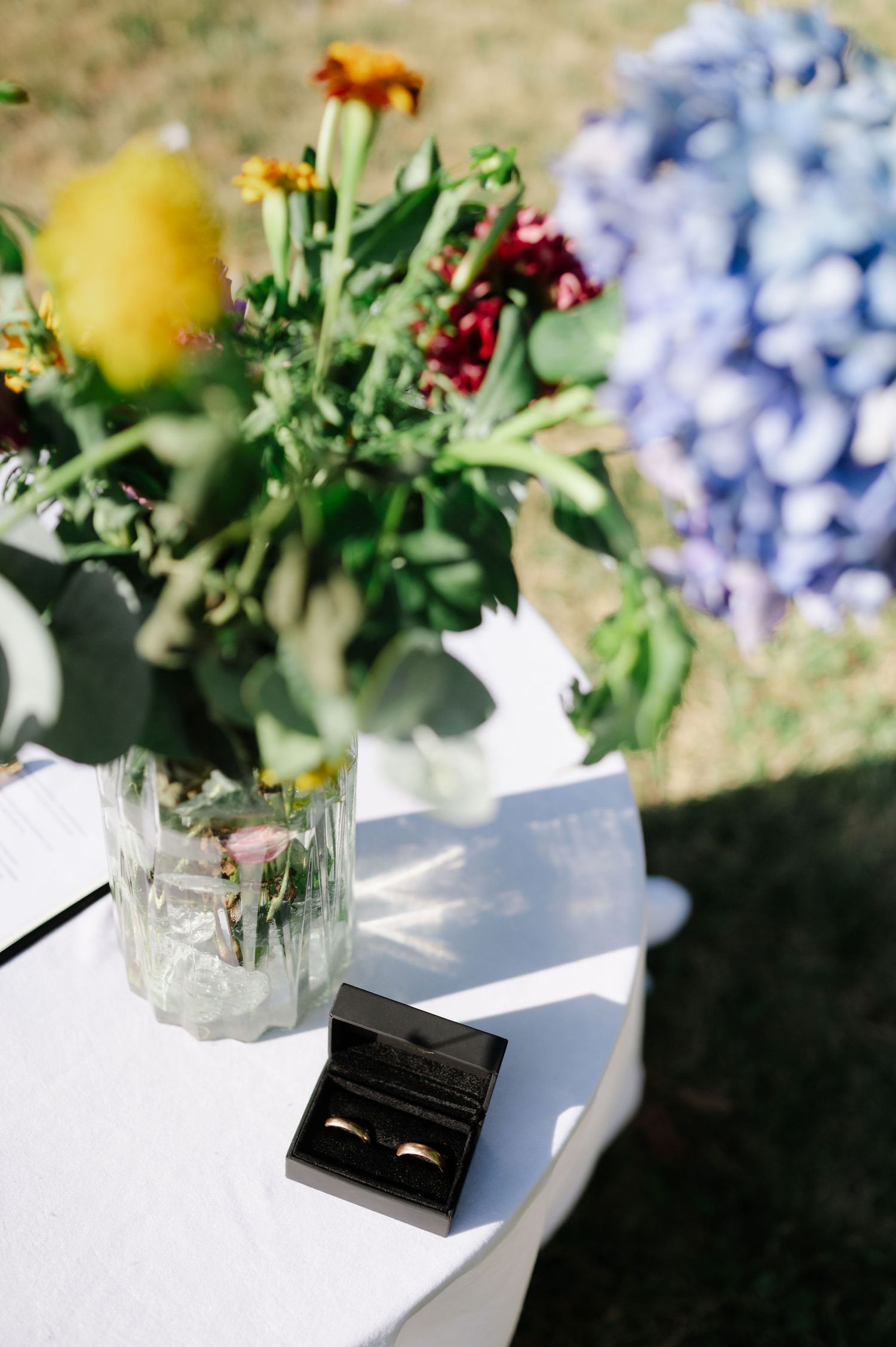Elegant floral centerpiece with hydrangeas and wedding rings on white table.