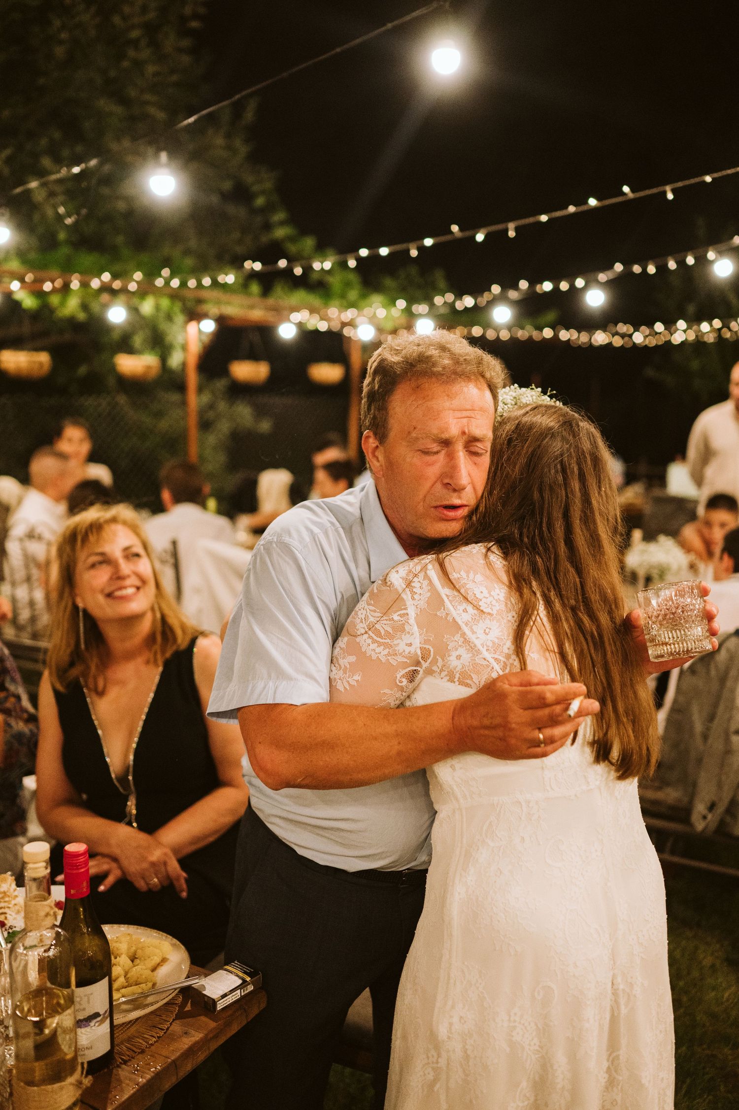 Wedding guests share joyful moments under string lights during an outdoor evening reception.