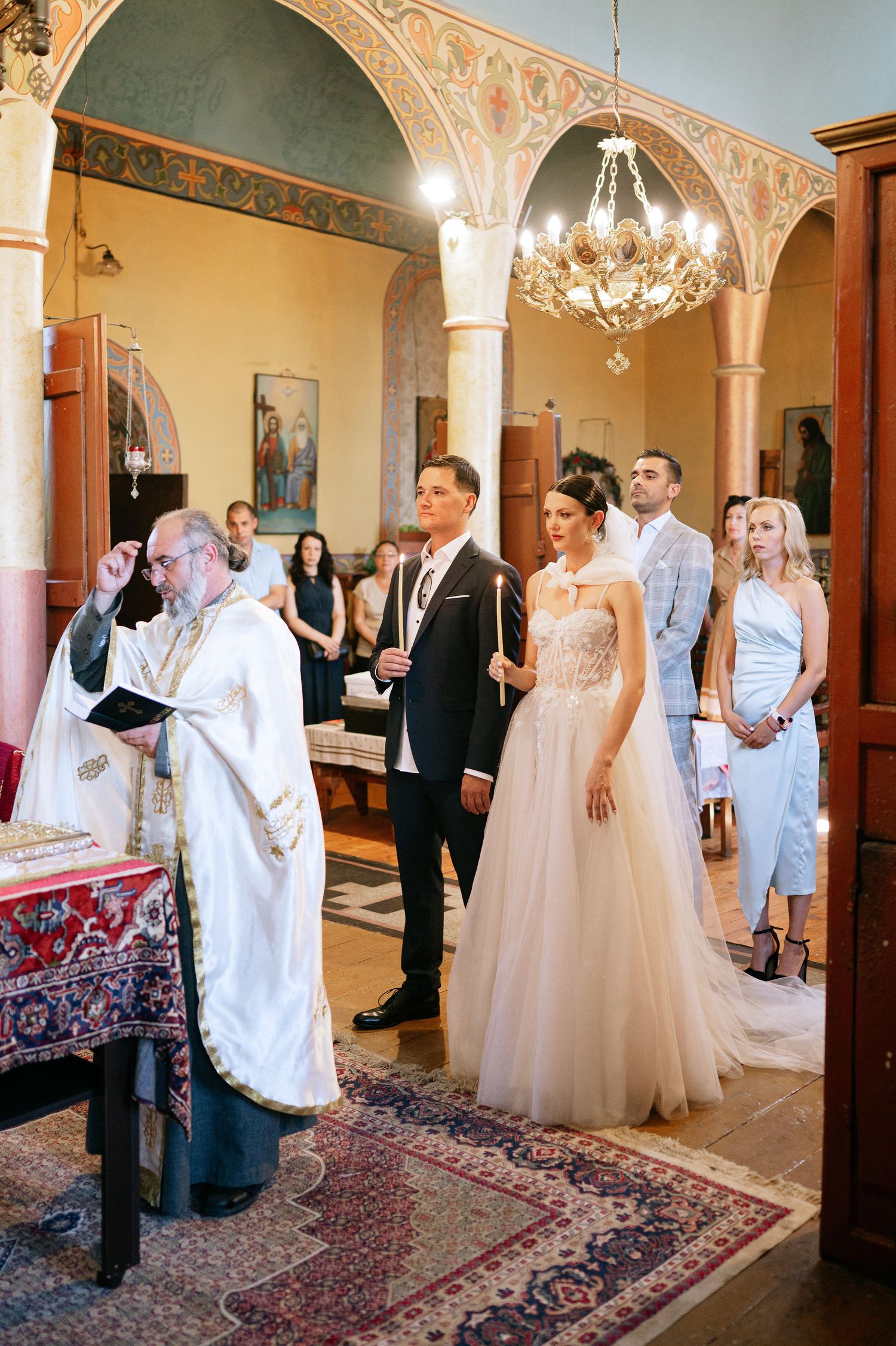Wedding ceremony taking place in an ornate church interior with decorative columns and elegant chandeliers.
