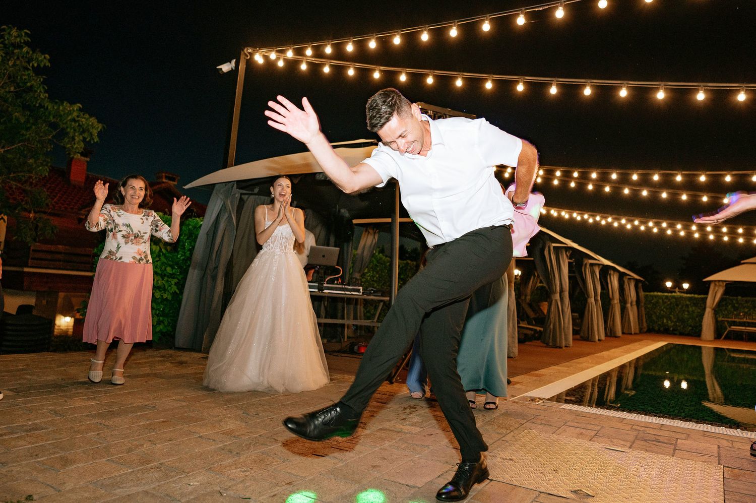 Guest performs dramatic dance move at outdoor wedding reception under string lights.