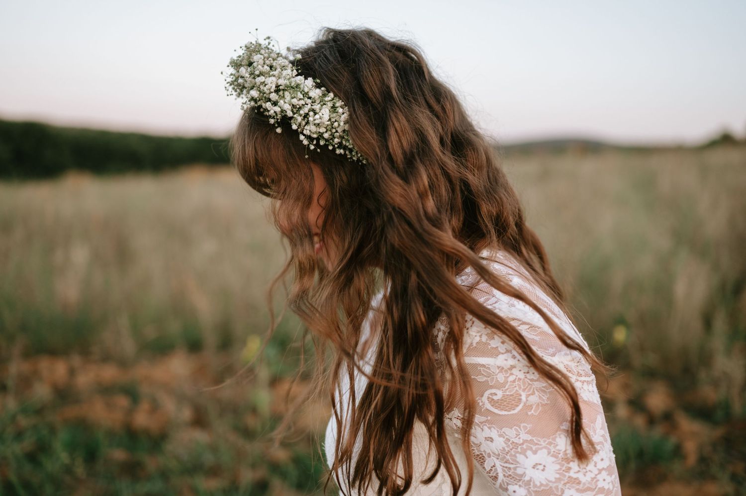 Bride wearing a delicate flower crown and lace dress poses in a sunlit field.