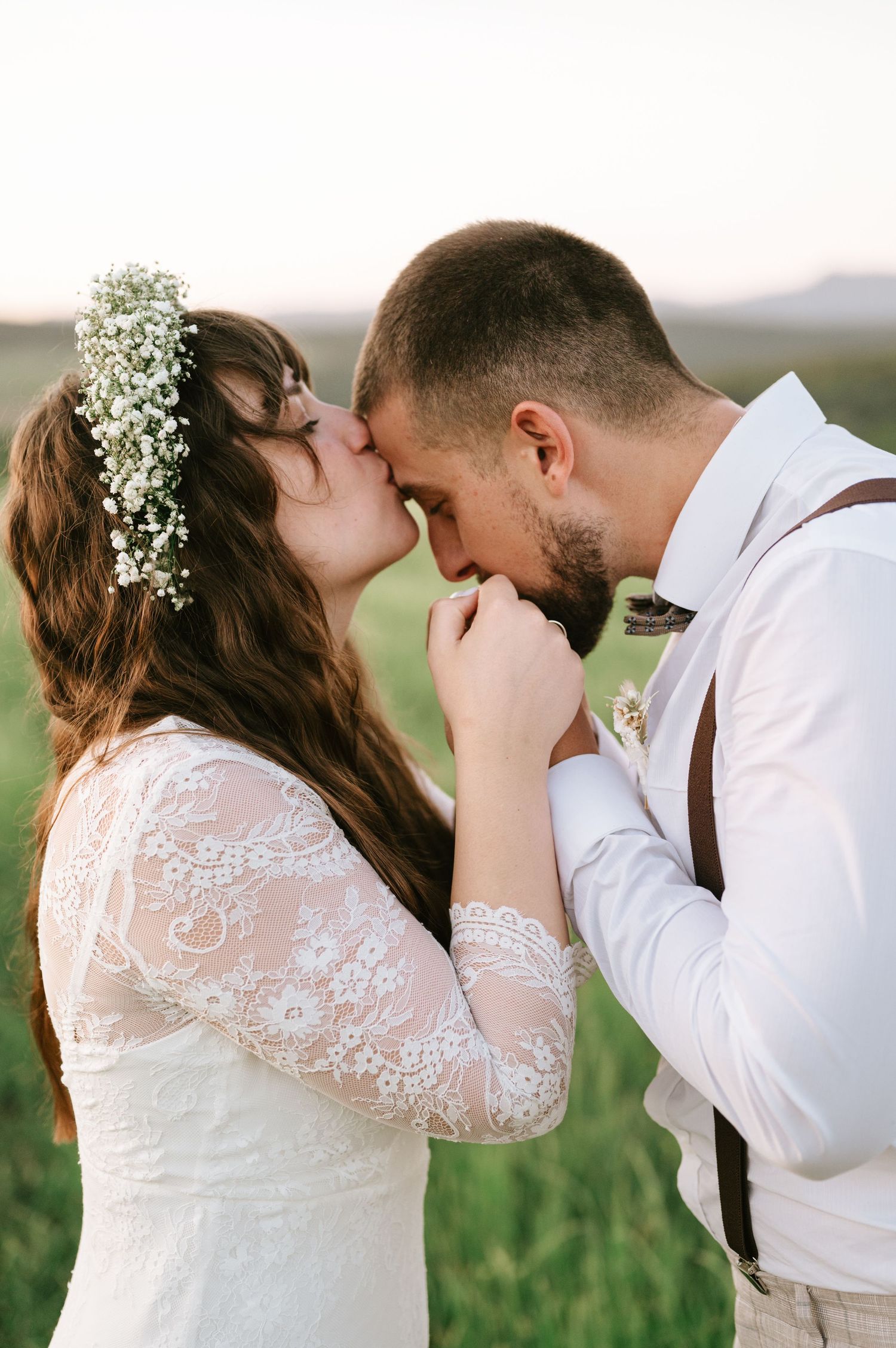 A romantic wedding portrait of a couple sharing an intimate moment in a meadow at sunset.