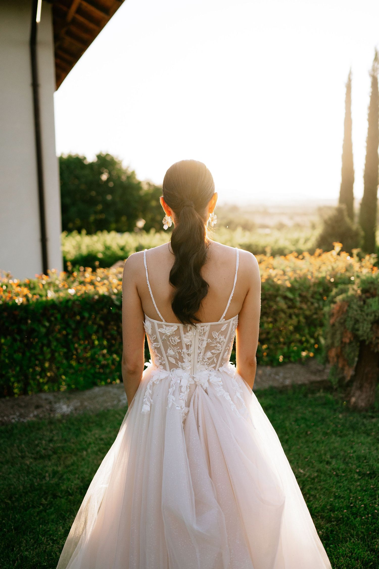 Back view of a wedding dress showing intricate lace detail against a garden landscape.