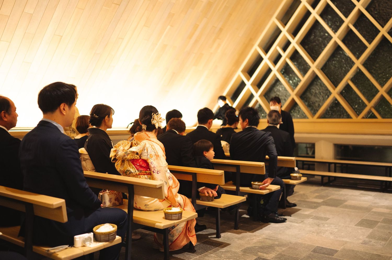 Attendees seated in rows at a modern venue with distinctive diagonal wooden lattice wall design.