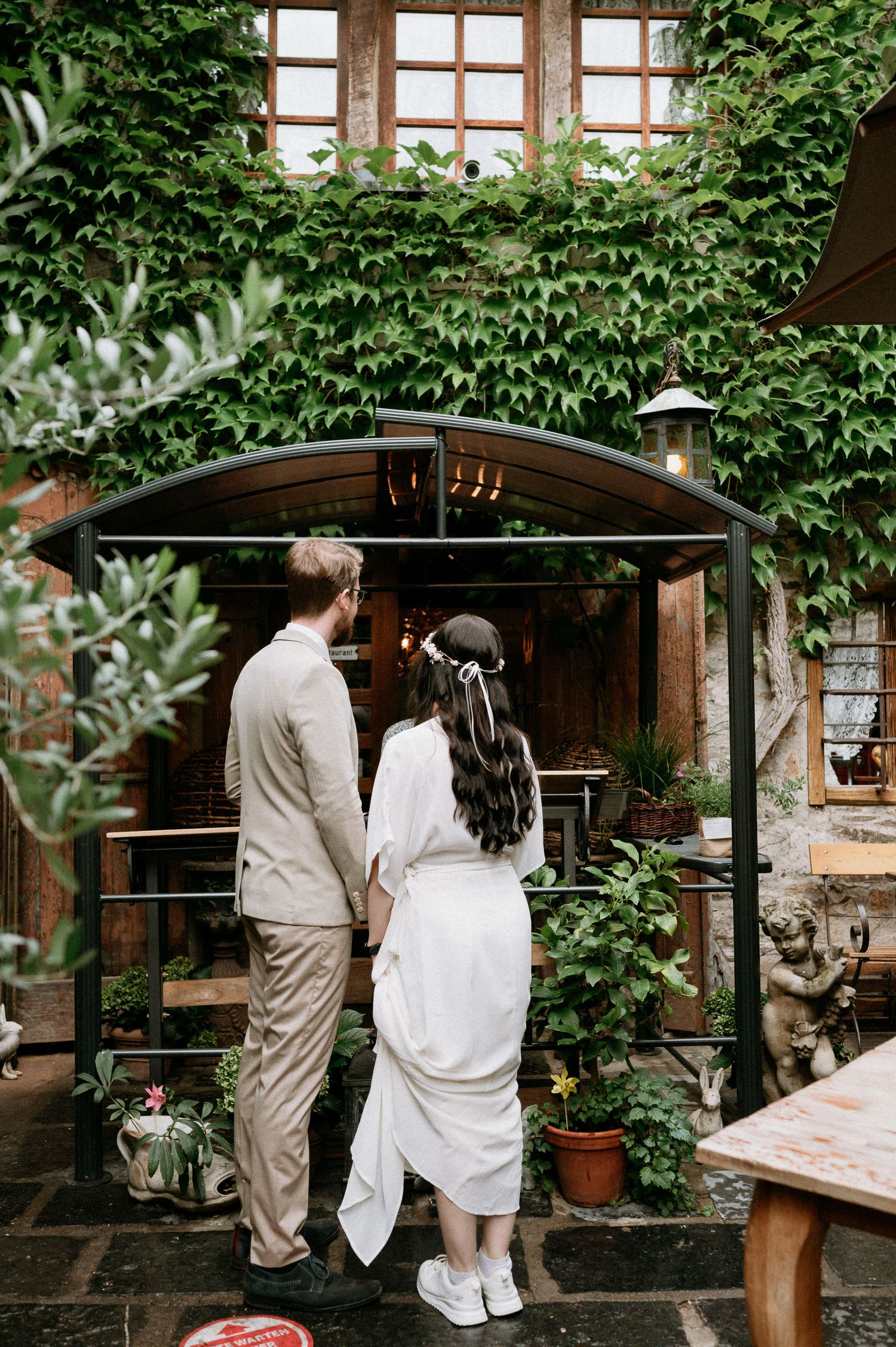 A couple stands beneath an ivy-covered archway entrance to a garden restaurant.