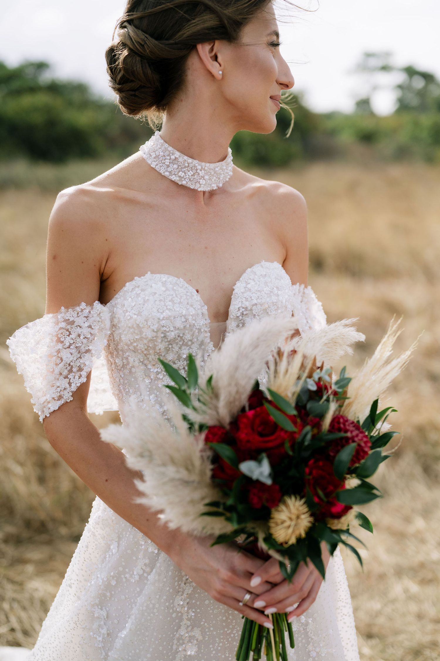 Detail shot of a bride's lace bodice and off-shoulder neckline with a burgundy and gold bouquet.