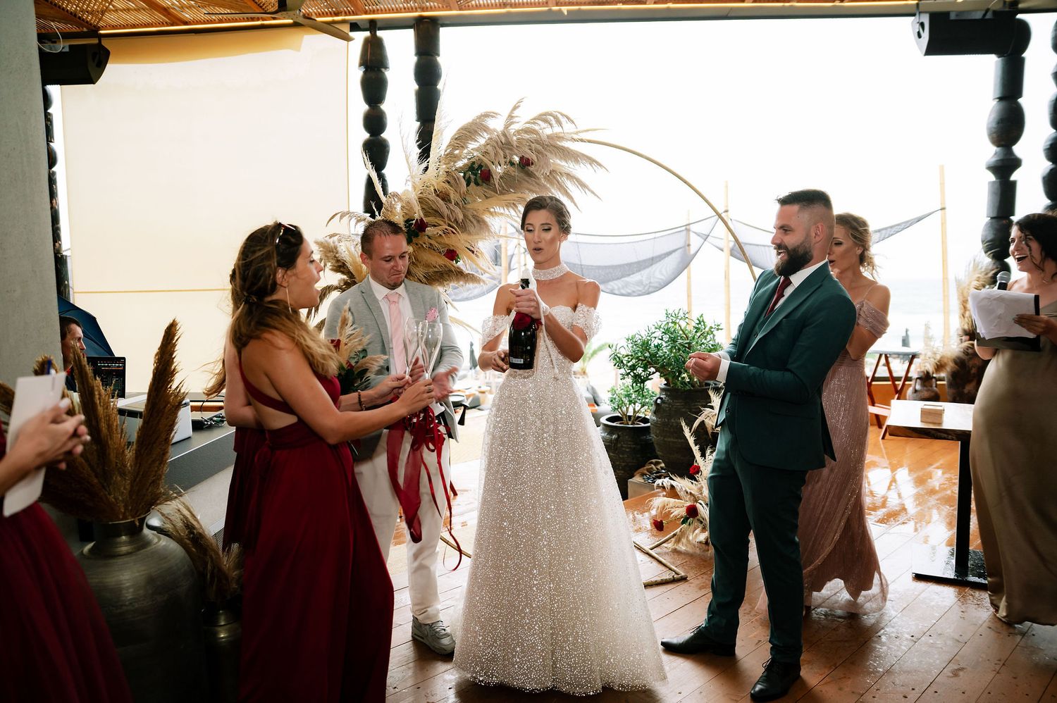 Wedding party celebrates during an intimate indoor ceremony with dried pampas grass decor and wooden beams overhead.