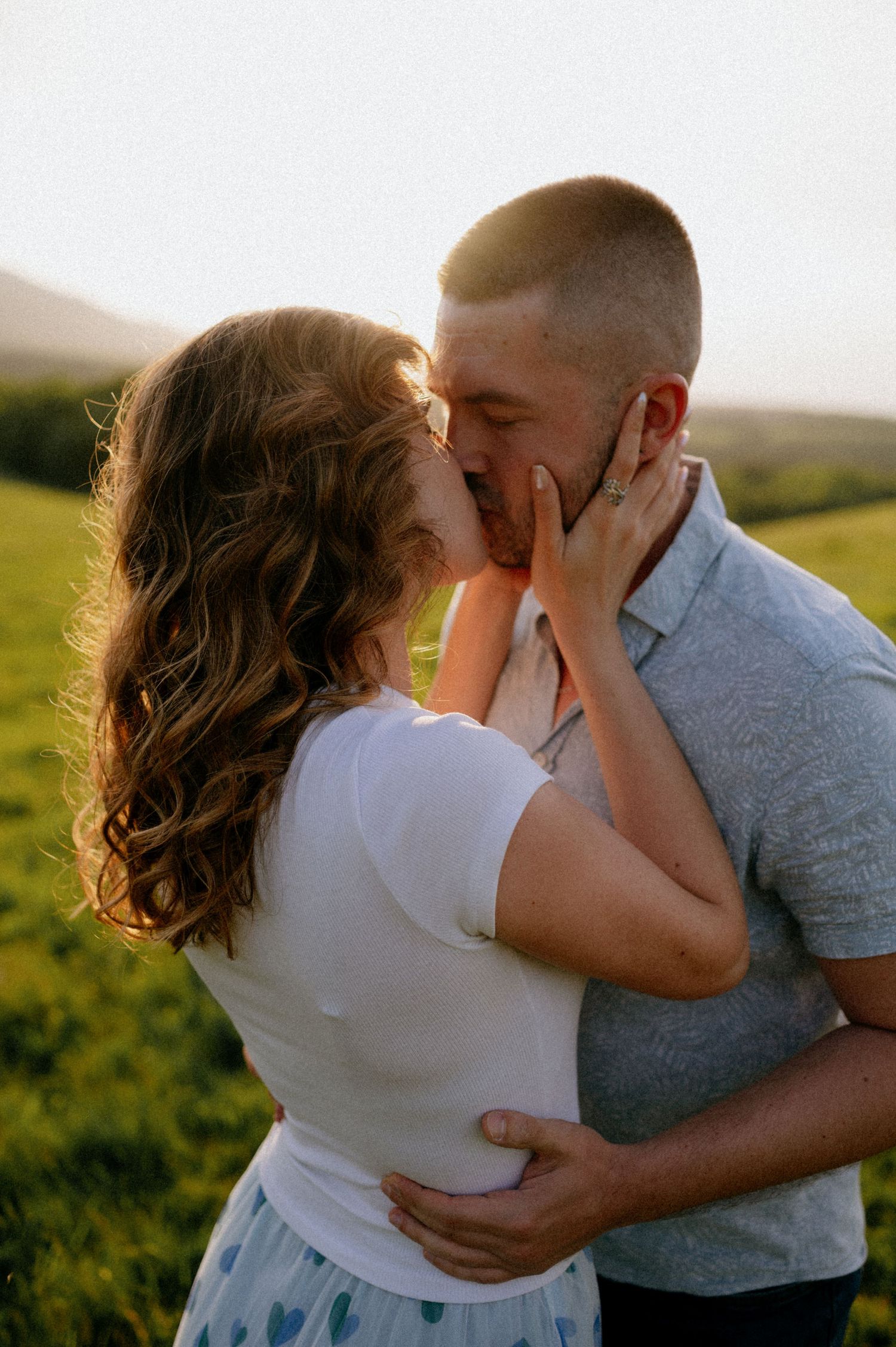 Two people share a tender moment while holding each other in a sun-drenched field.