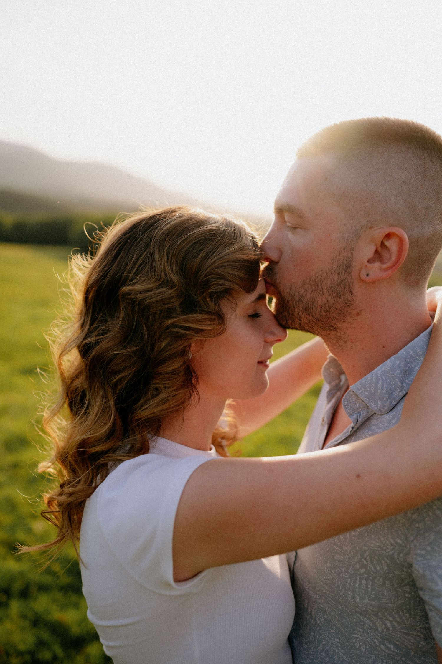 A romantic couple shares an intimate kiss while standing in a sunlit meadow.