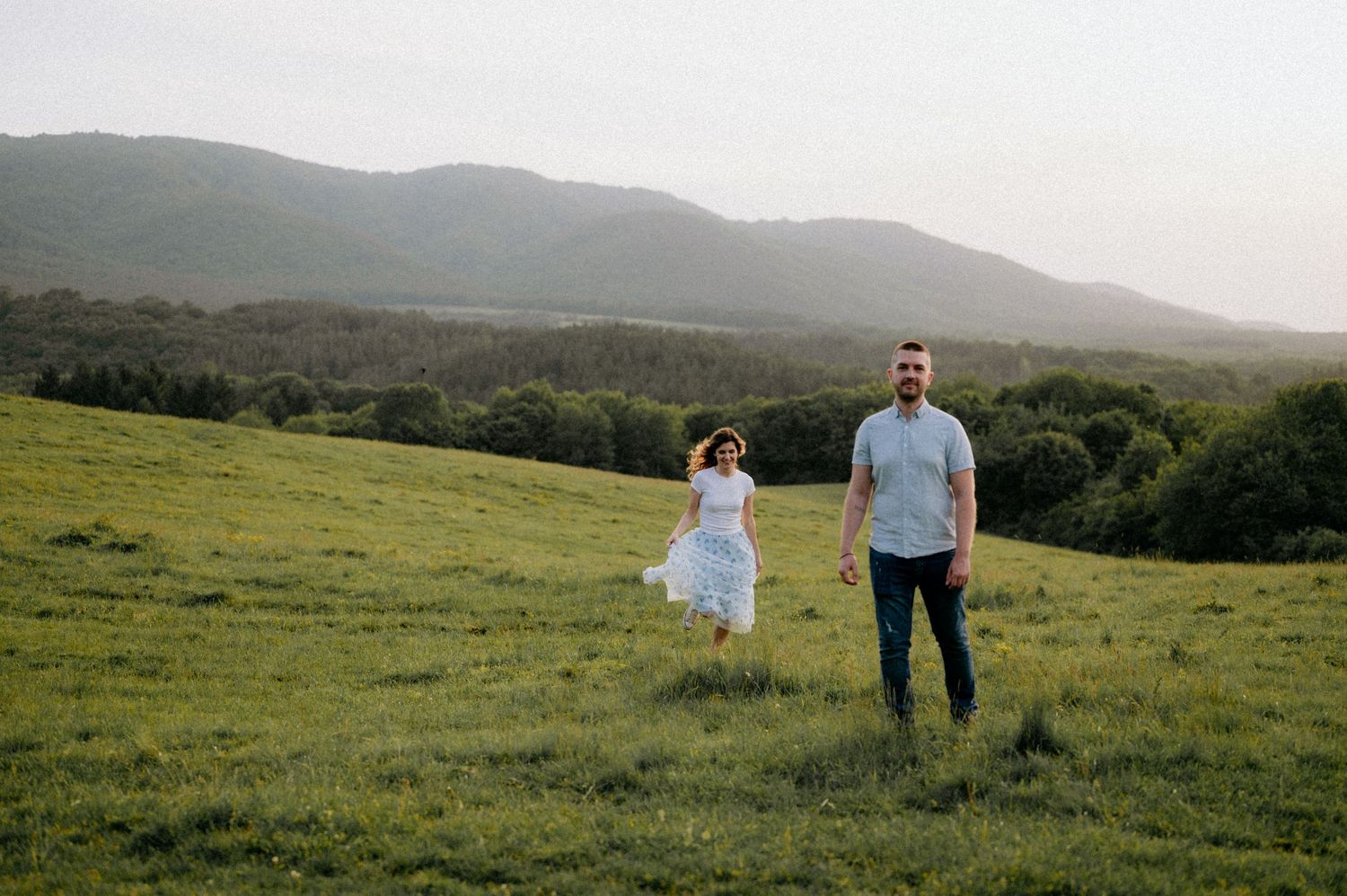 Couple strolling through a scenic mountain meadow at dusk.