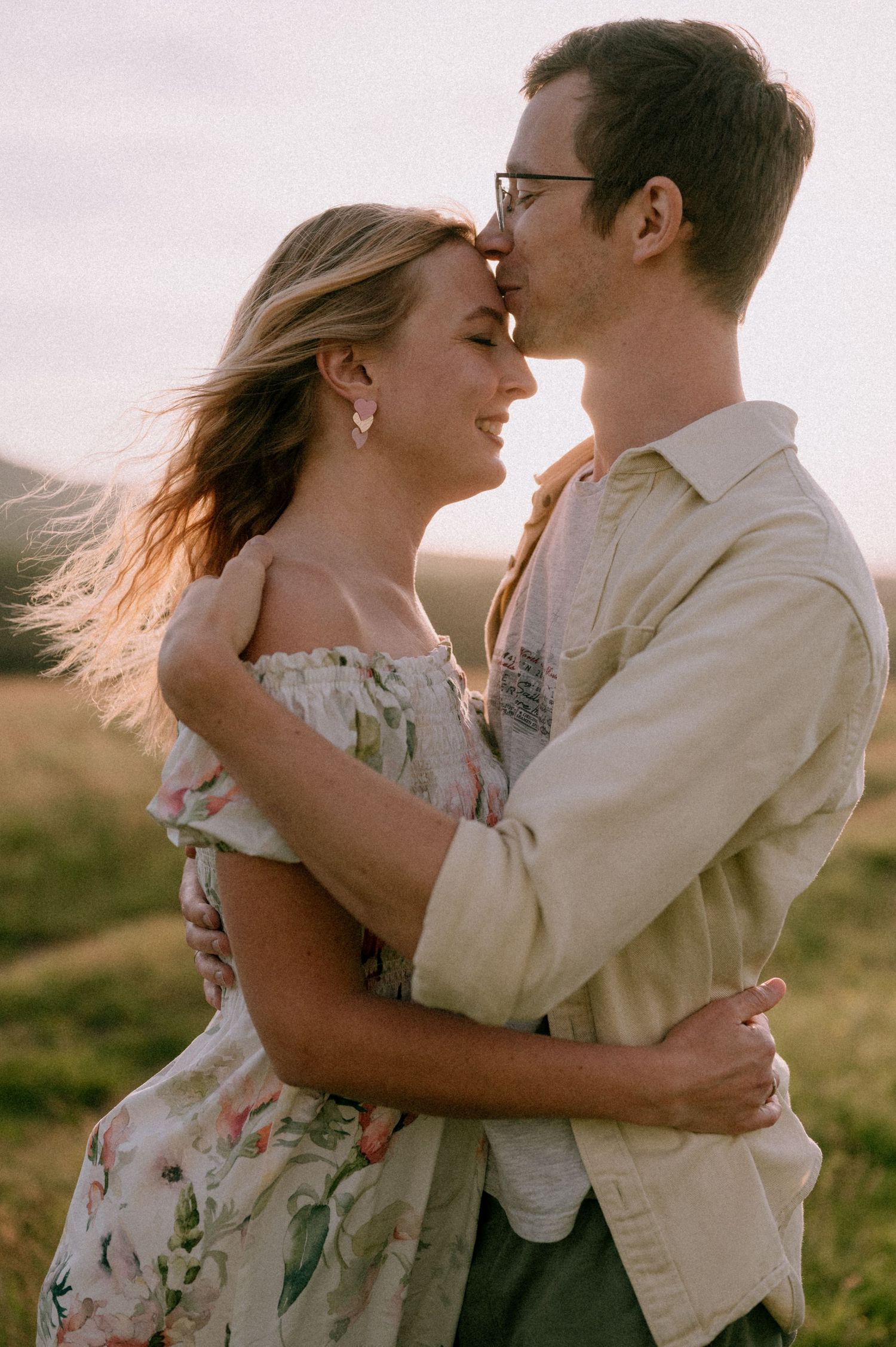 Intimate couple embracing in golden sunlight against scenic mountain landscape.