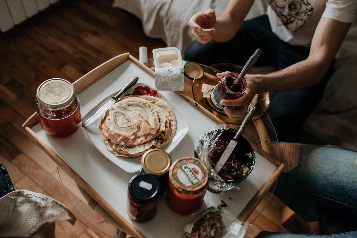 Hands spread homemade jam on fresh bread at a rustic wooden table during breakfast preparation.