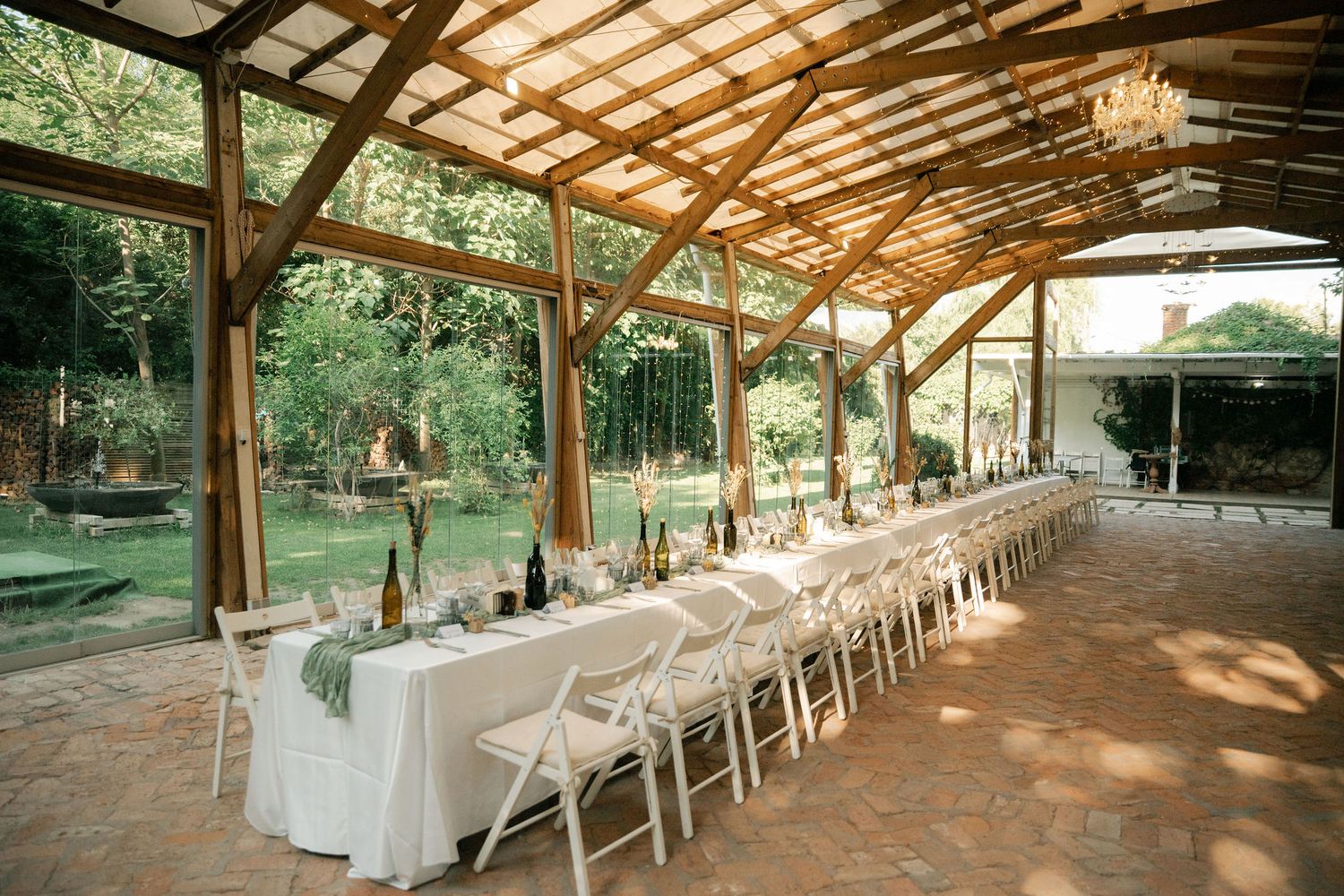 Rustic outdoor wedding venue with wooden beams and white chairs set up in rows under a covered pavilion.