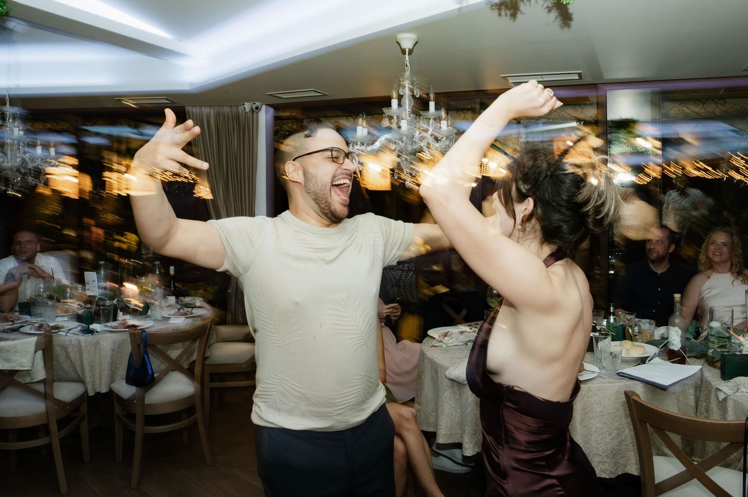People dancing and celebrating at a reception party with arms raised in joyful movement.