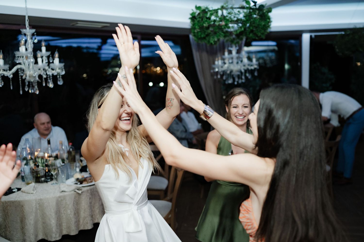 Wedding guests dance and celebrate on a dance floor during an evening reception under white tents and chandeliers.
