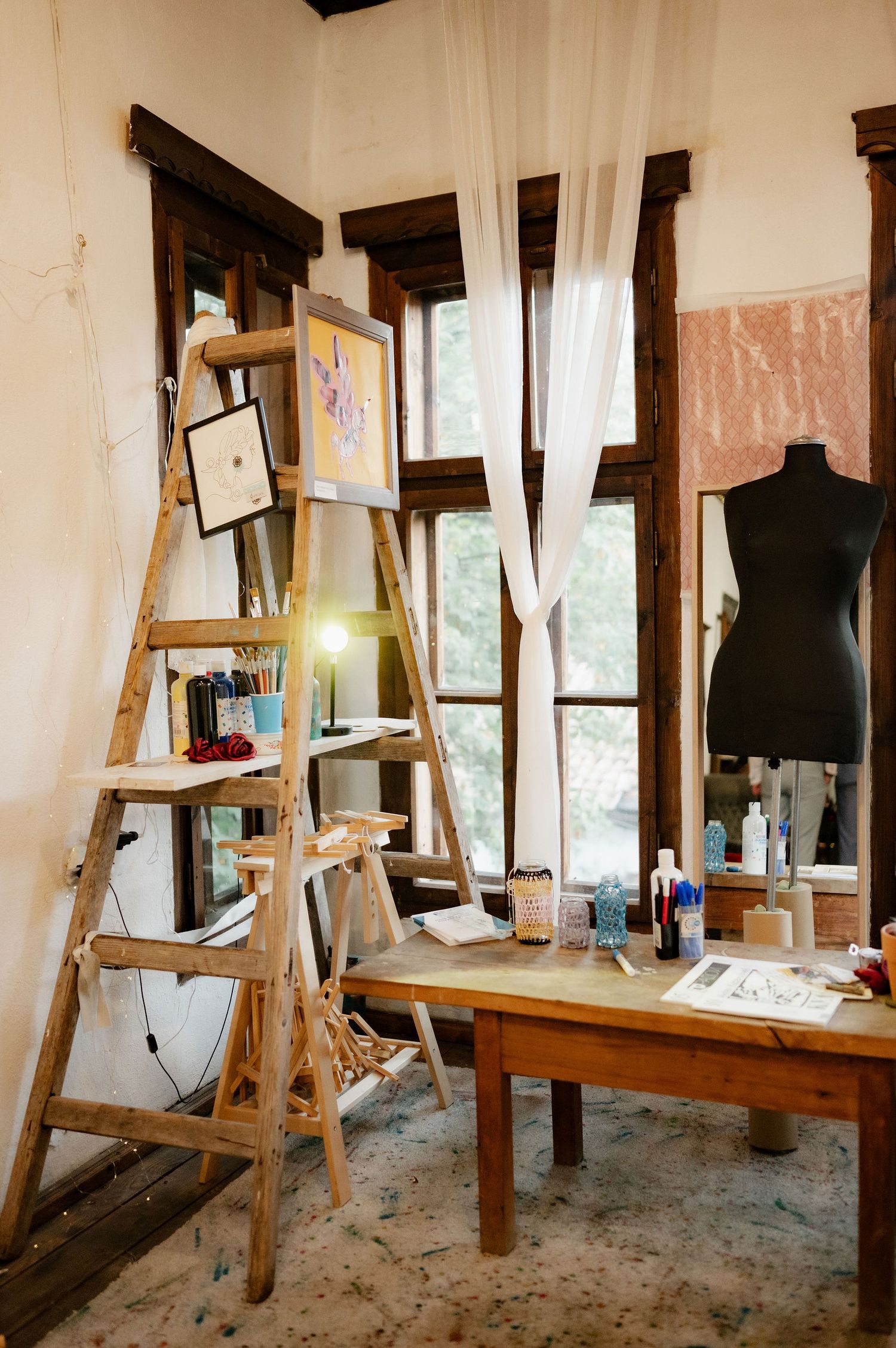 Rustic art studio interior with wooden easels, dress forms, and natural light streaming through windows.