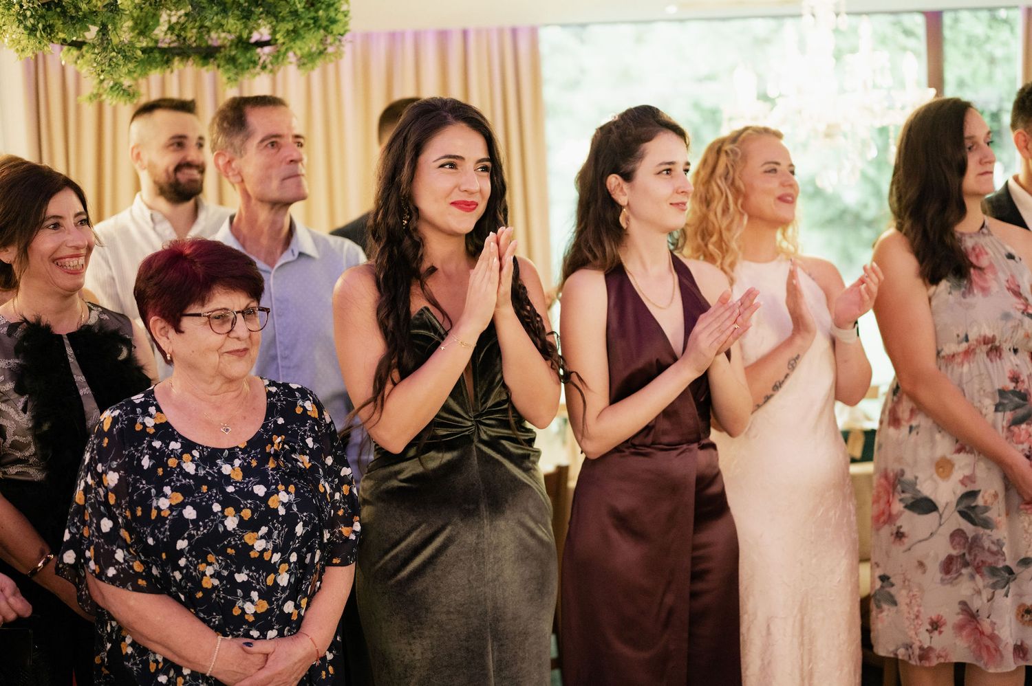 A group of wedding guests stand in a row clapping and celebrating during a reception ceremony.