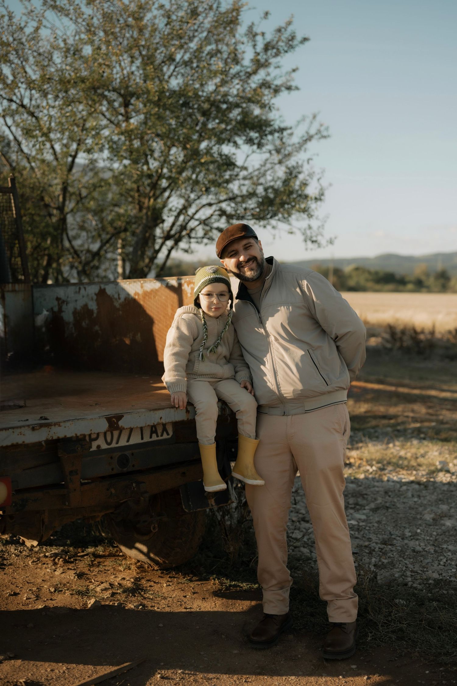 Two people in matching beige outfits lean against a rustic wooden bench in warm evening sunlight.