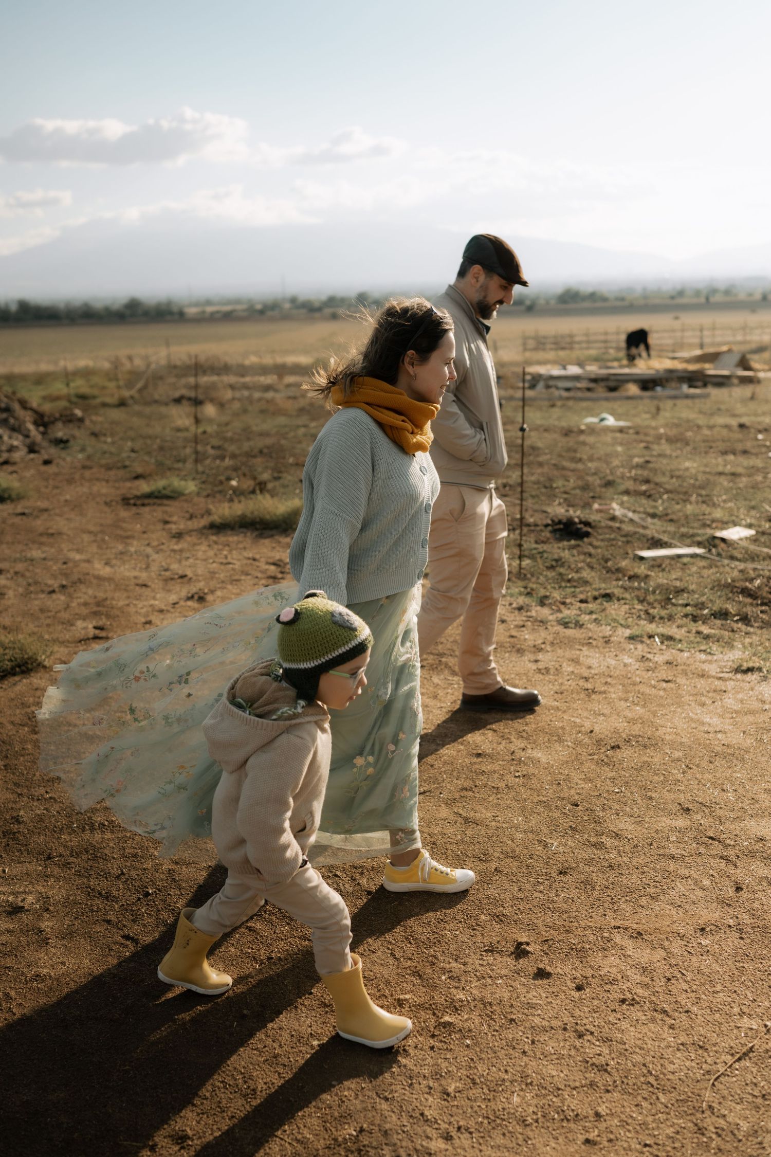 Three people in casual attire stand together on dusty ground with mountains visible in the distance.