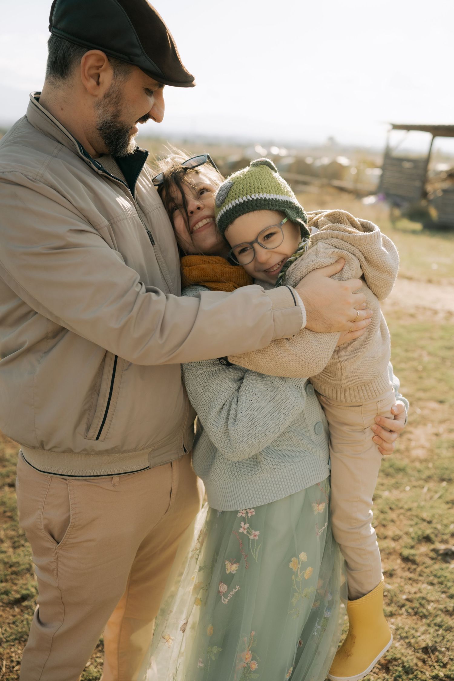 A couple embraces tenderly outdoors in soft natural lighting while wearing casual earth-toned clothing.