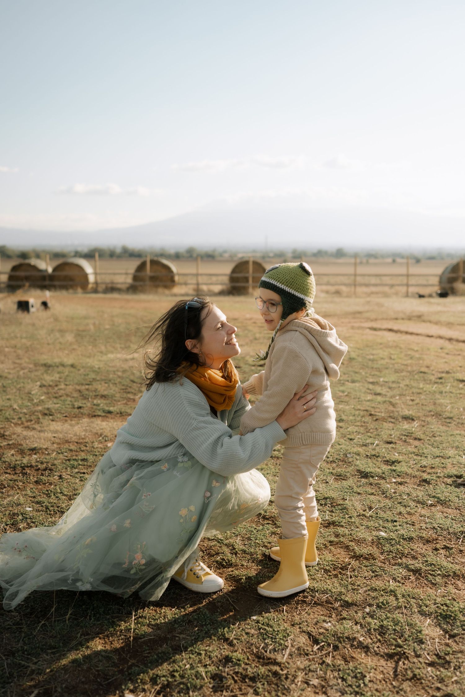 A parent and child share a tender moment playing together in an open field at sunset.
