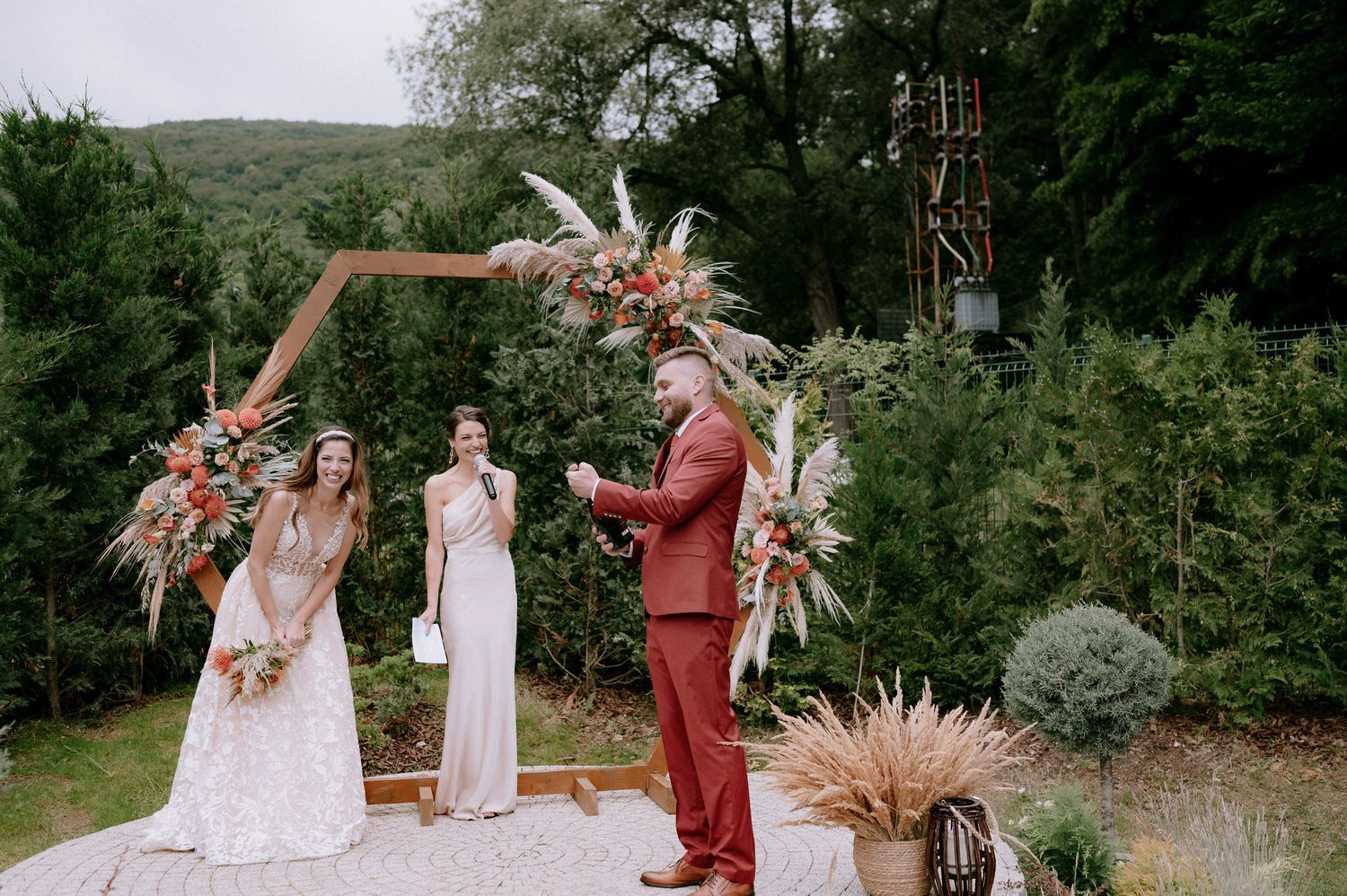 Outdoor boho wedding ceremony with pampas grass decor and rustic wooden chairs in a natural forest setting.