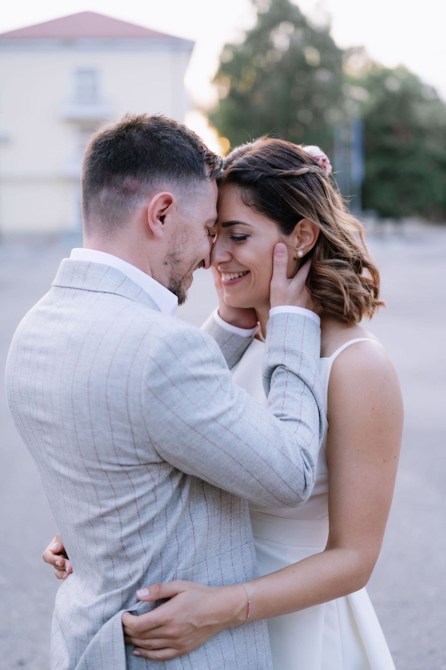 A tender moment between newlyweds sharing an intimate embrace outdoors at sunset in elegant wedding attire.