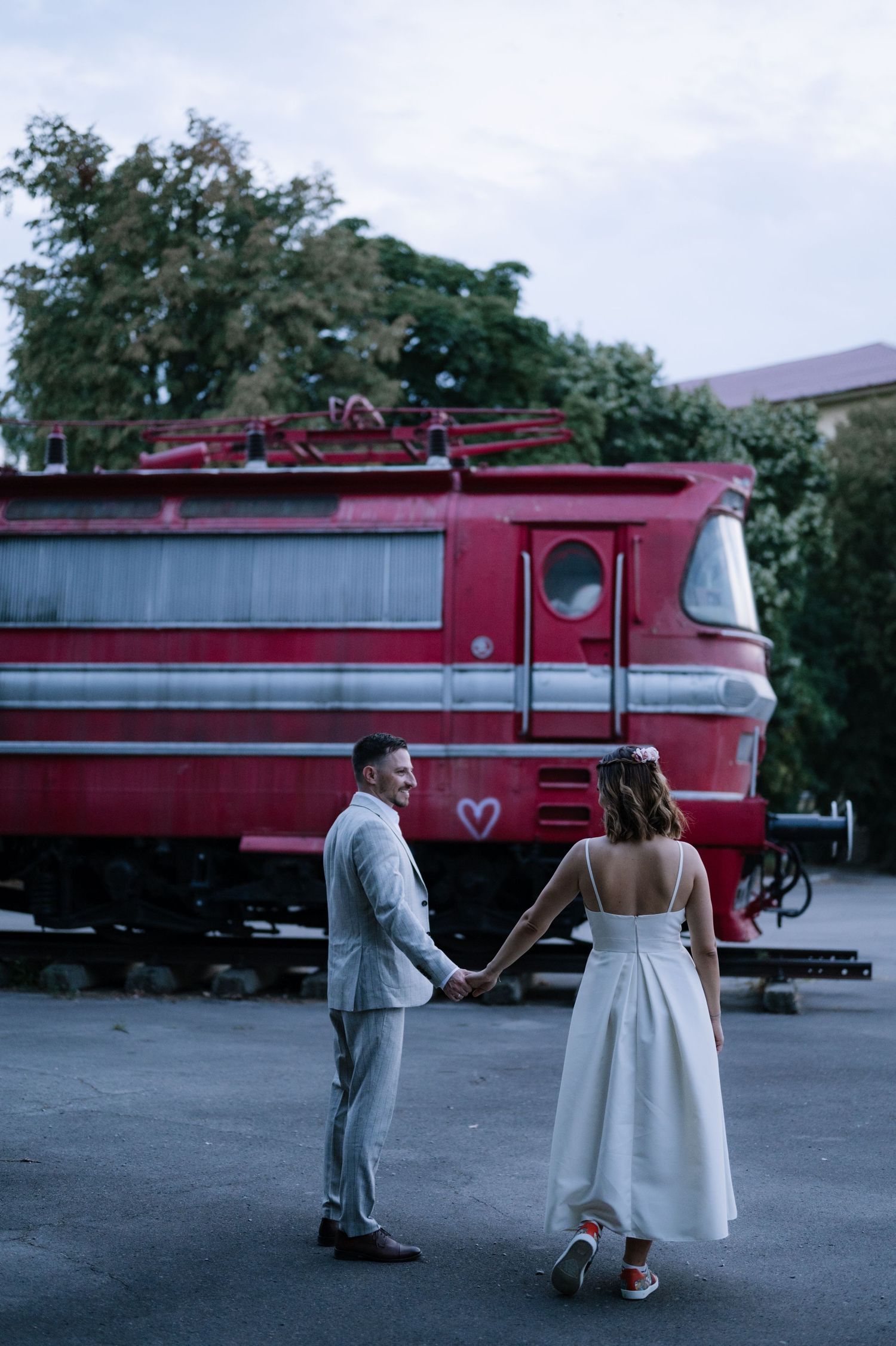 A romantic proposal scene unfolds in front of a vintage red train at a railway station.
