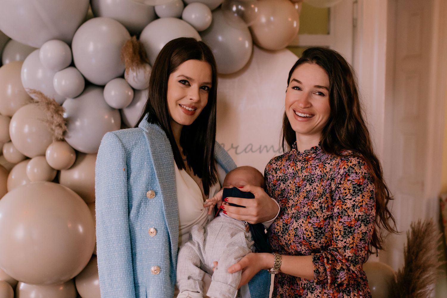 Friends celebrate at a baby shower with gray balloon arch decorations in the background.
