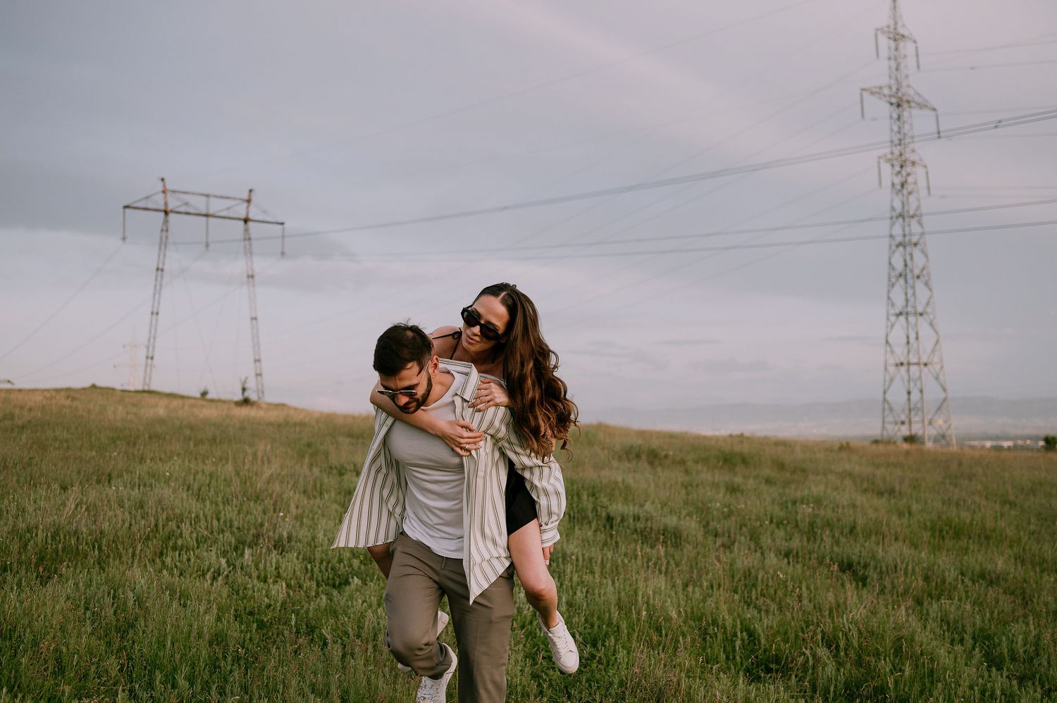 A couple shares a romantic moment in a grassy field beneath power lines at sunset.